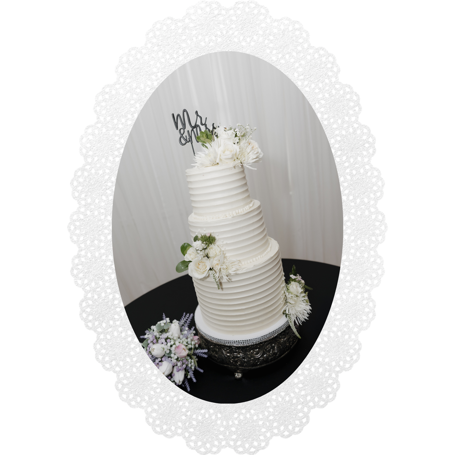 Elegant four-tier white wedding cake with floral accents and Mr. & Mrs. topper on a black stand.