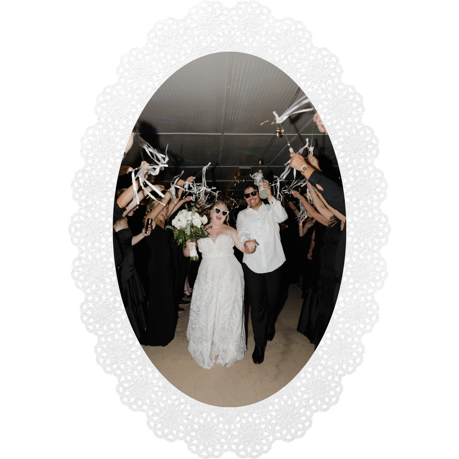 Bride and groom exit wedding ceremony through guest tunnel with streamers, bride in white lace gown holding bouquet.