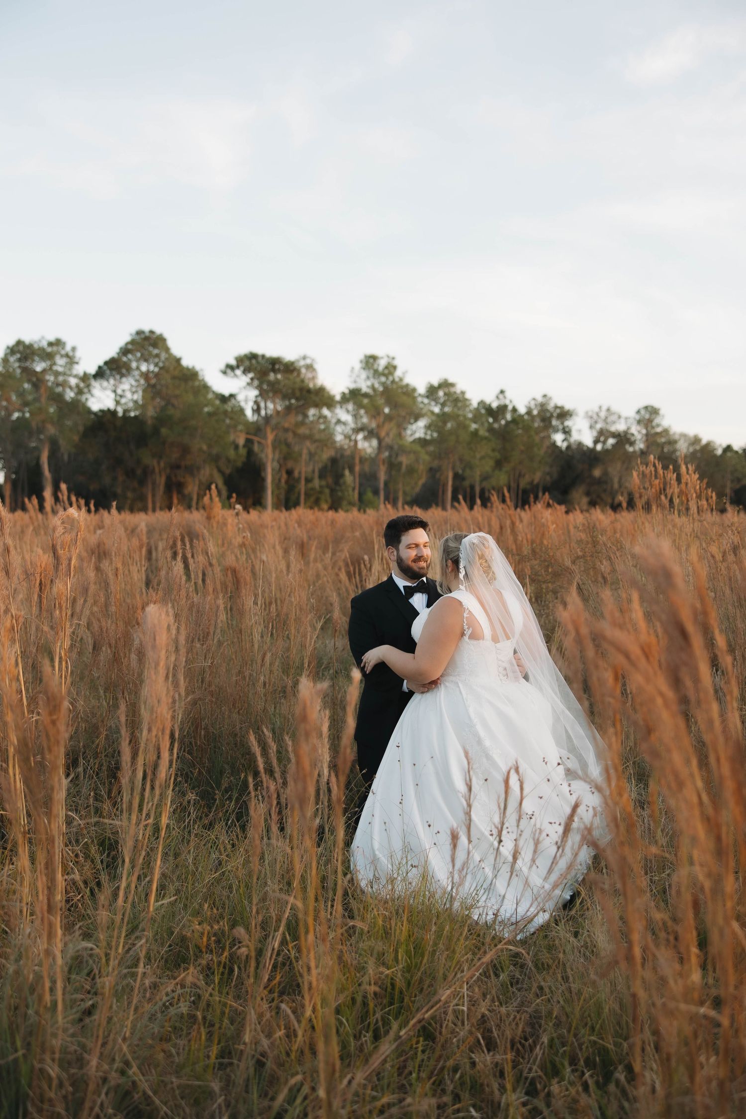 Newlyweds pose together in a field of golden grass during sunset for romantic wedding portraits.