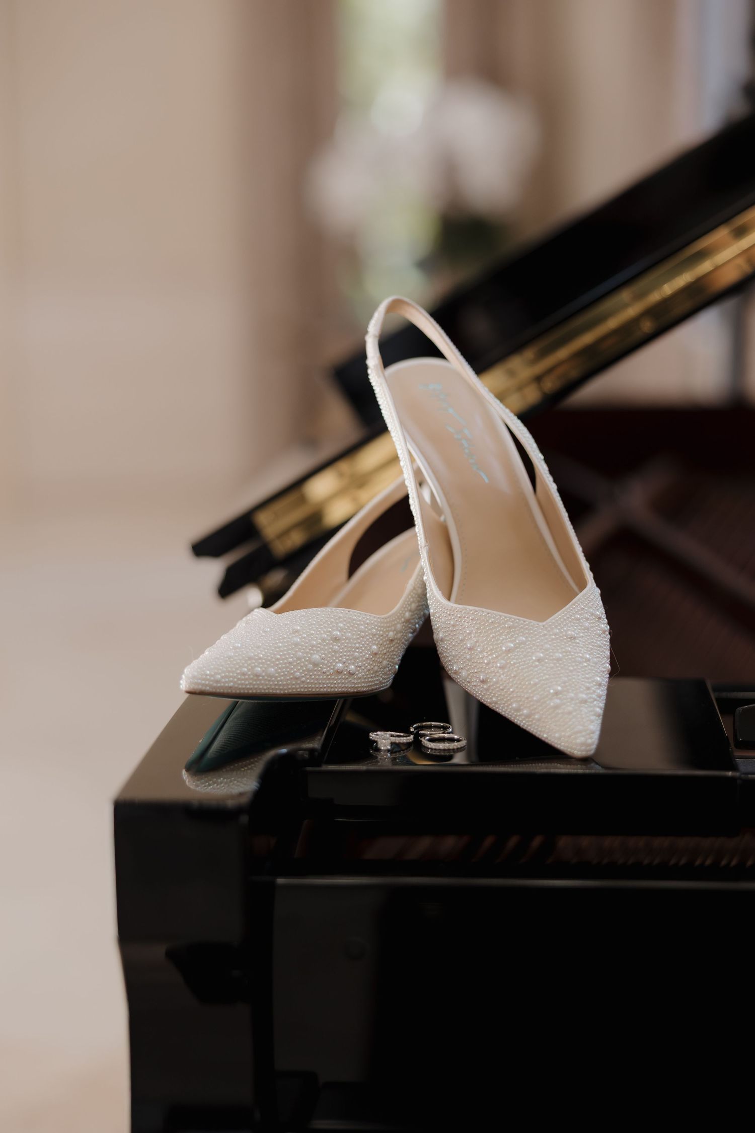 White lace bridal shoes elegantly displayed on a black grand piano, creating a romantic wedding detail shot.
