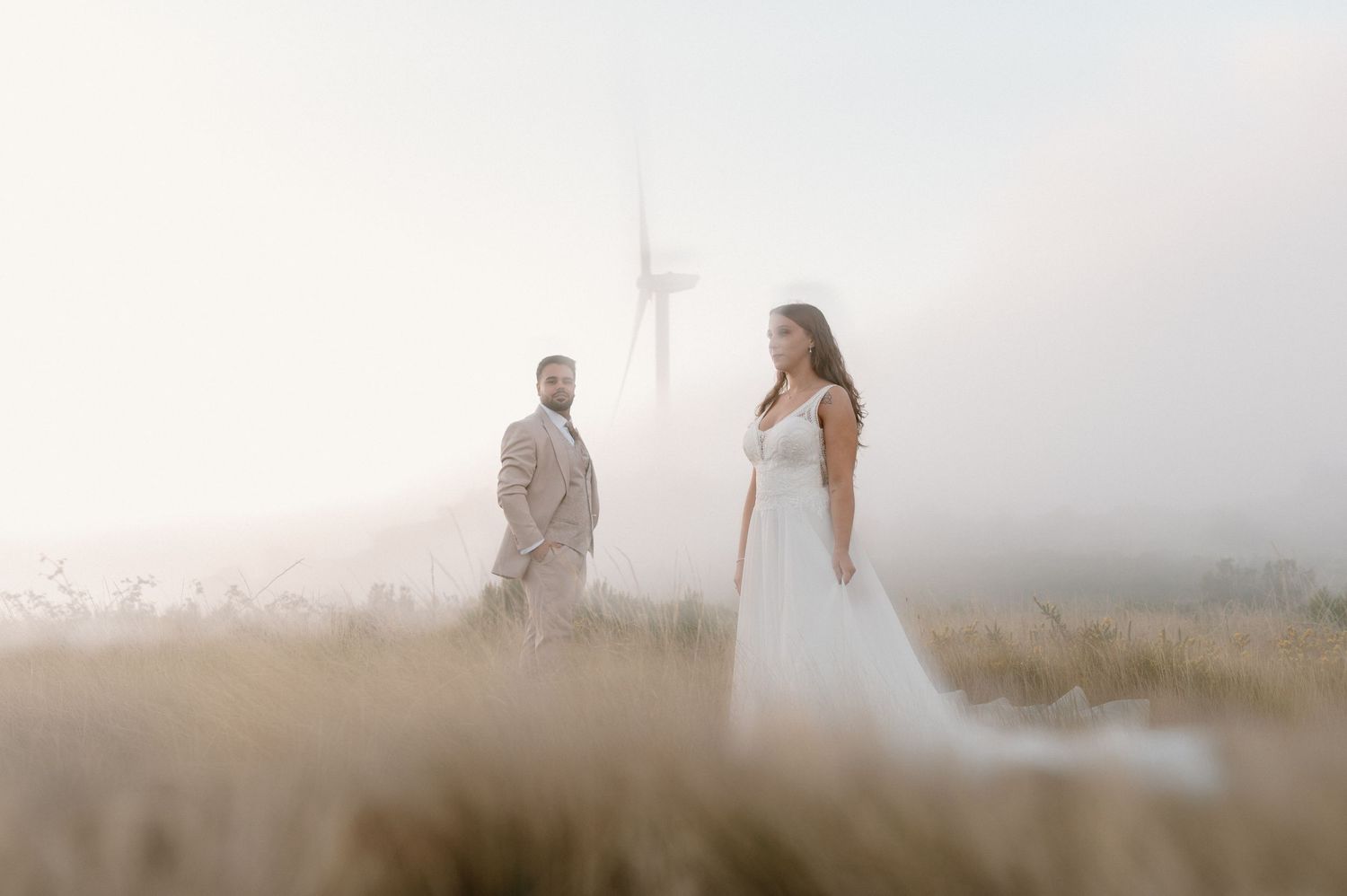 Silhouetted figures stand in foggy field at sunset creating ethereal romantic atmosphere.