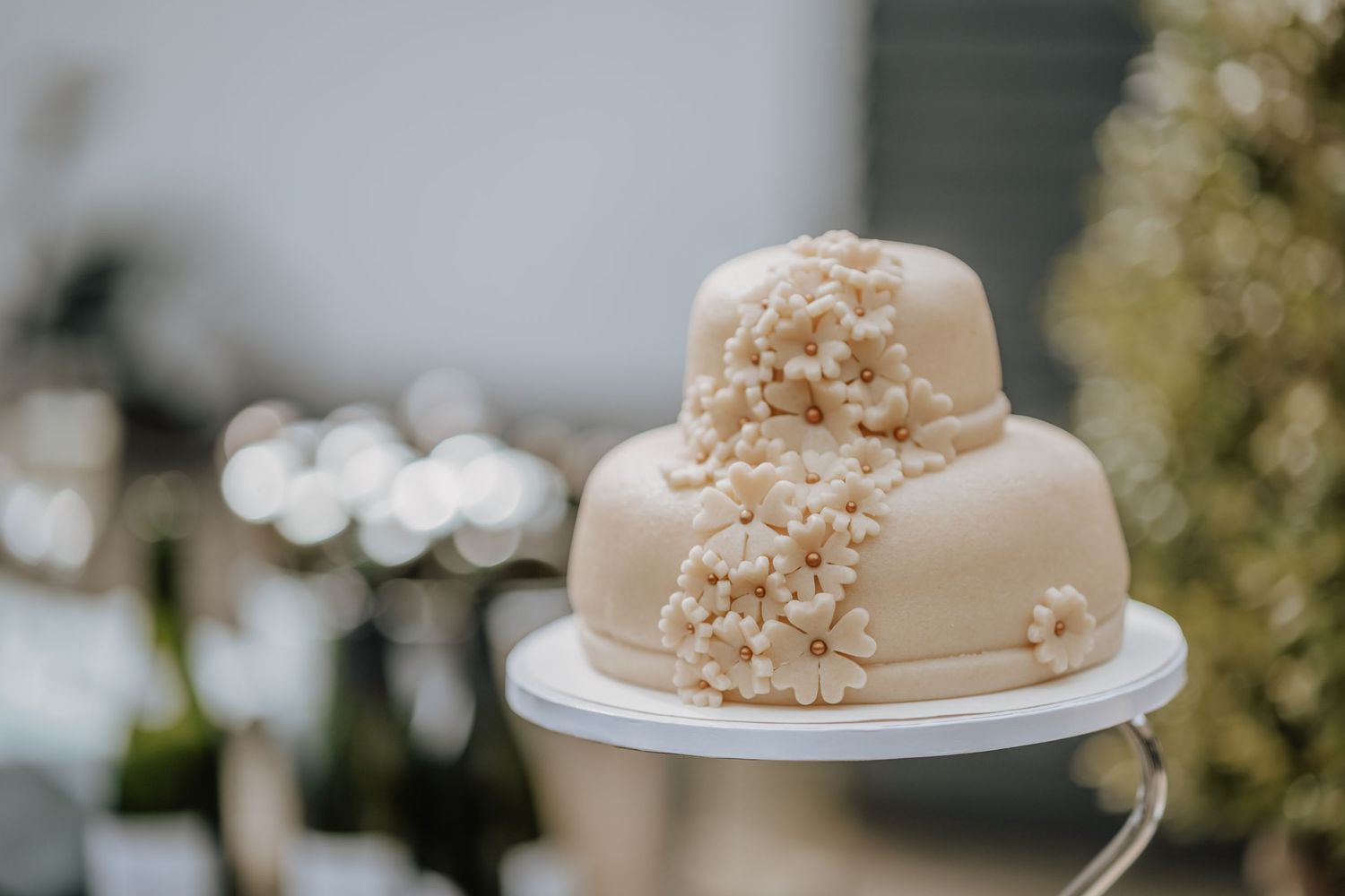 Two-tiered elegant white wedding cake decorated with cascading small floral details in cream colors on a white cake stand.