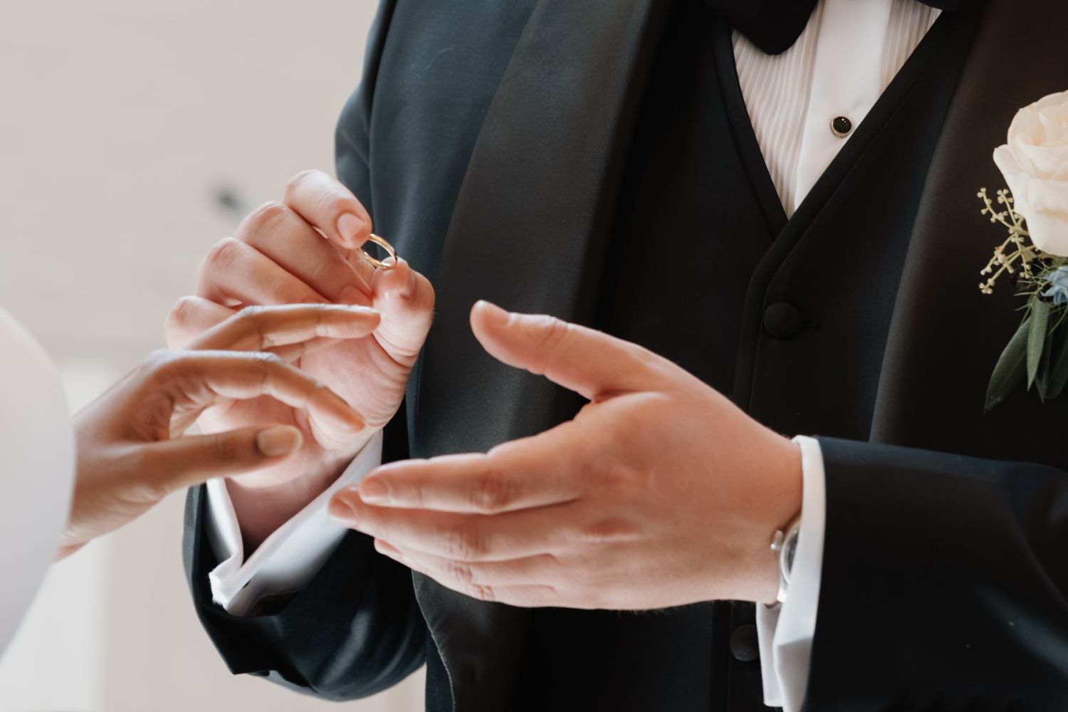 A close-up shot shows hands exchanging rings during a wedding ceremony, with a black suit and boutonniere visible.