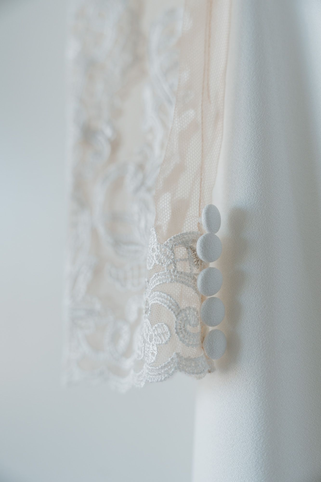 Close-up detail of delicate white lace and button closures on a wedding dress sleeve.