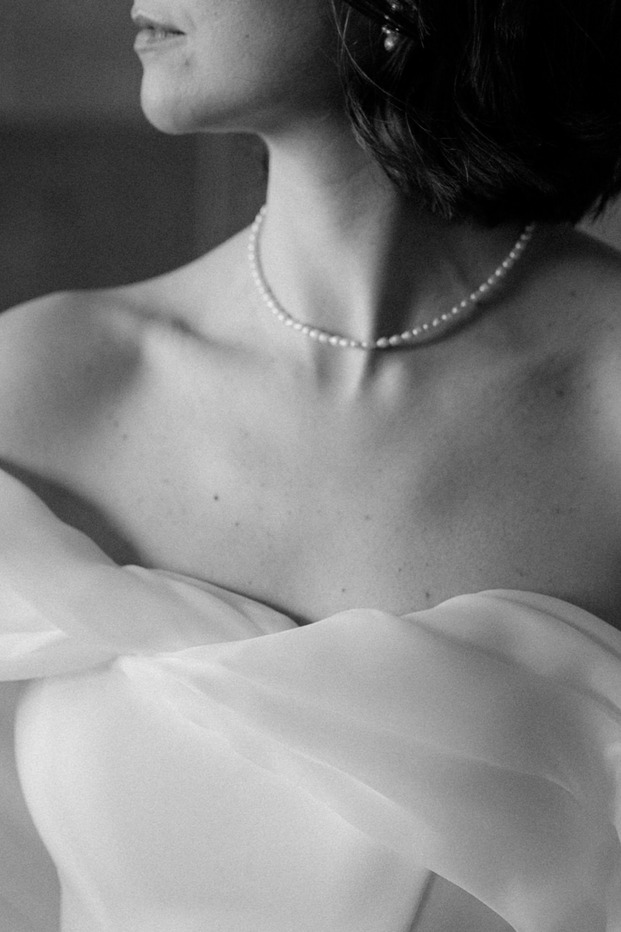 Black and white photo of a bride wearing a pearl necklace and strapless white gown, elegant and timeless.