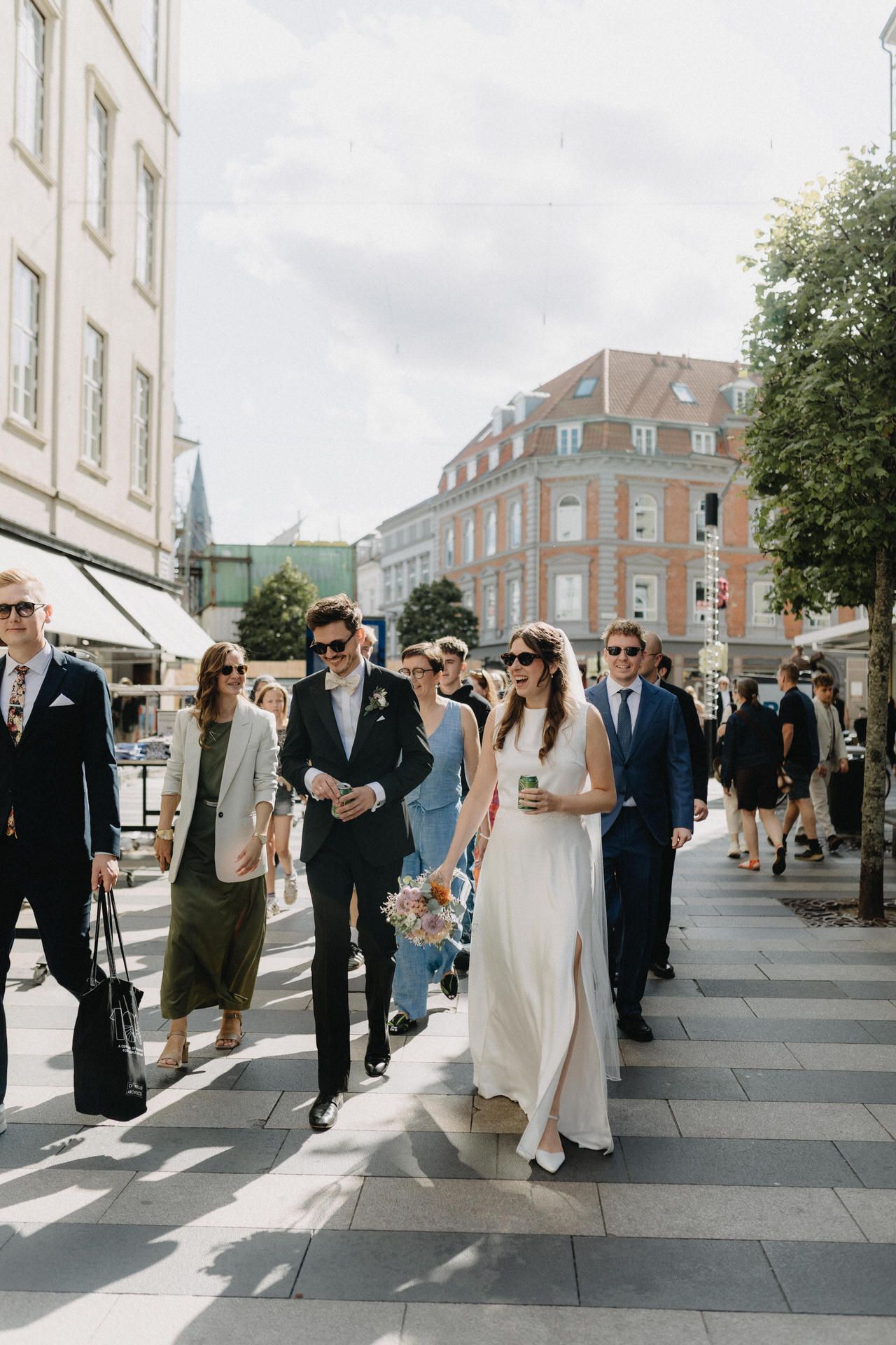 Wedding party walking down city street in elegant formal attire during outdoor celebration.