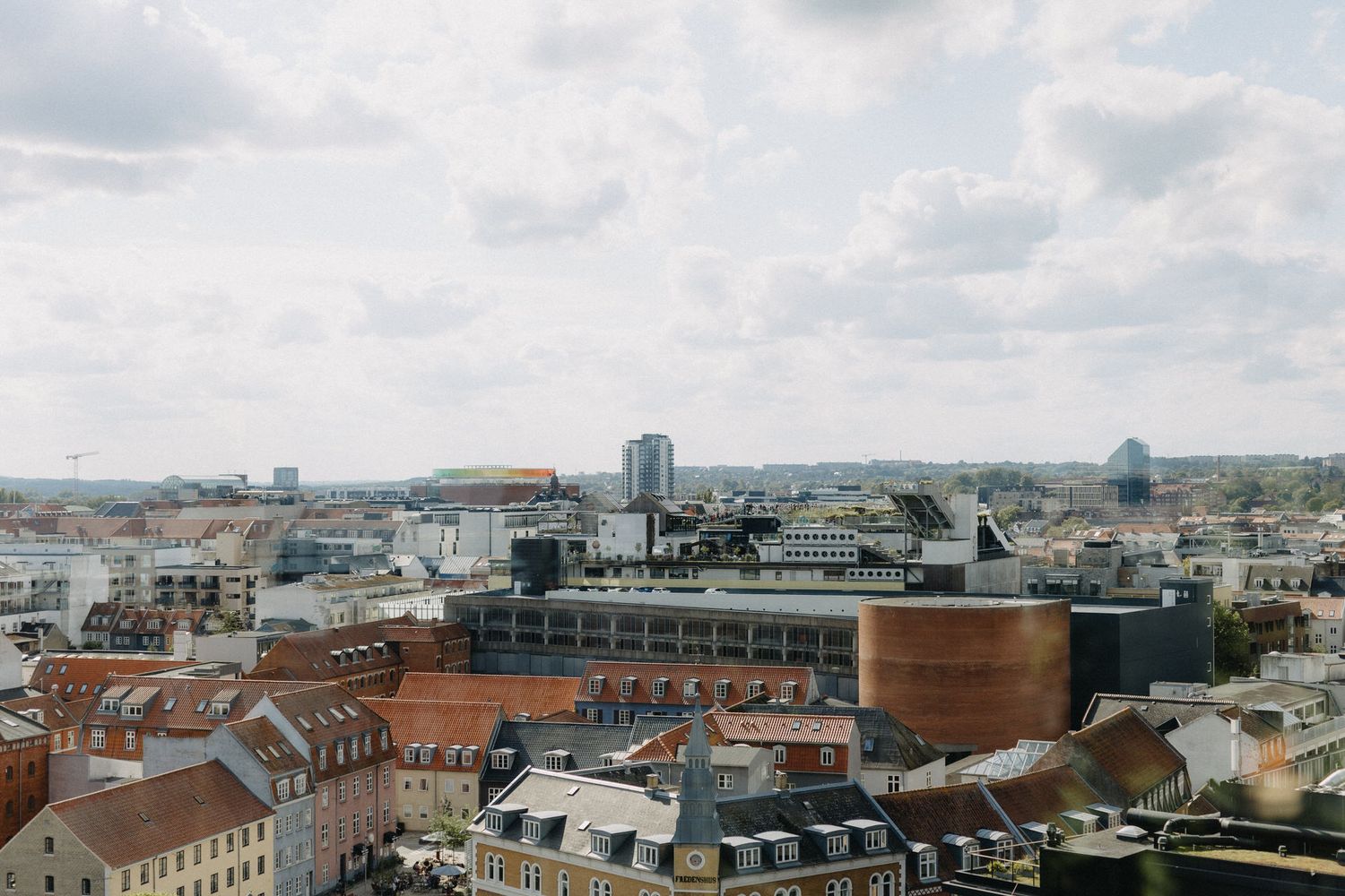 Panoramic aerial view of Prague's historic cityscape with red-tiled roofs and modern buildings in the distance.