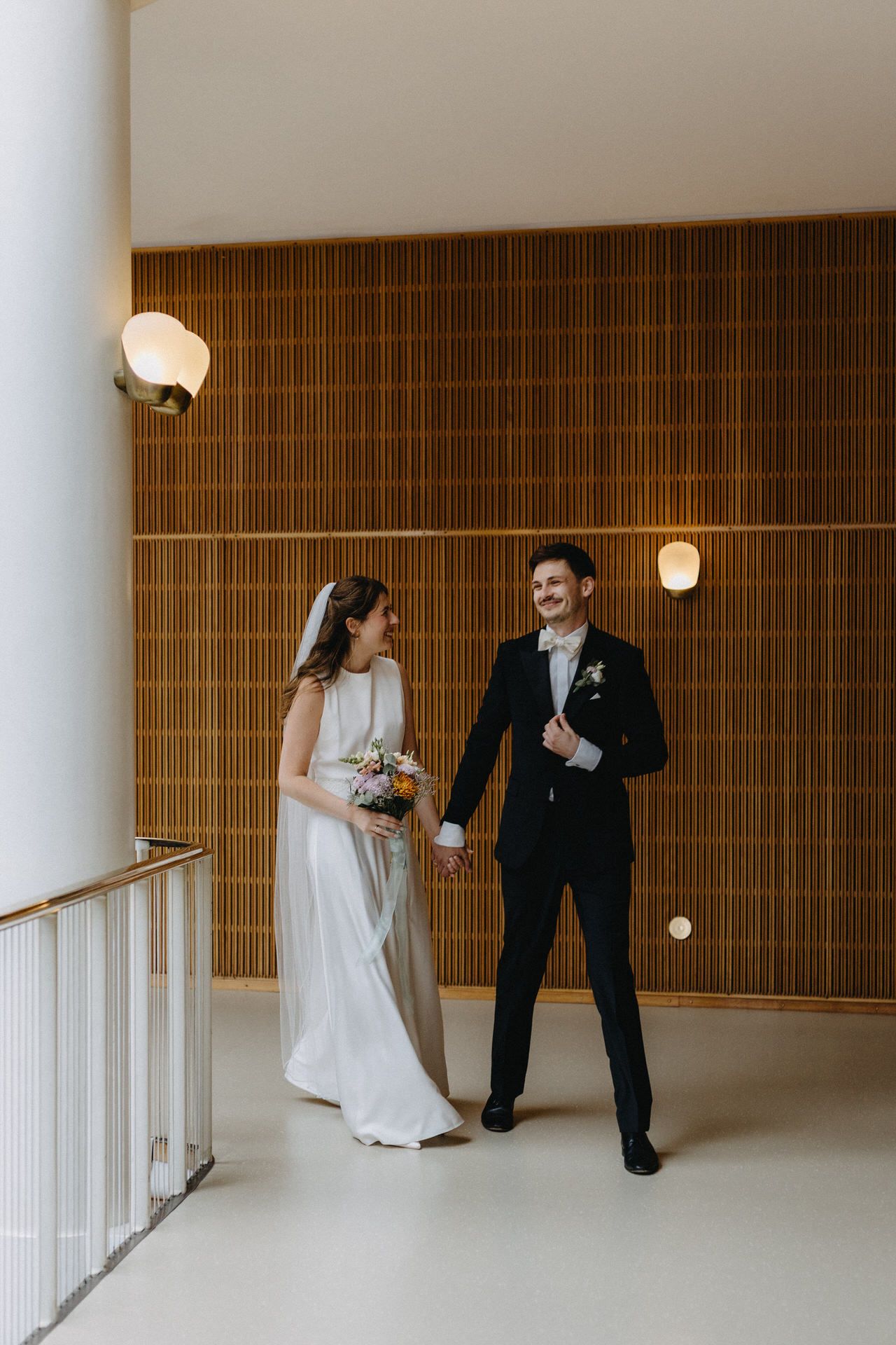 A couple shares a joyful moment in a modern hallway with wood paneled walls and geometric light fixtures.