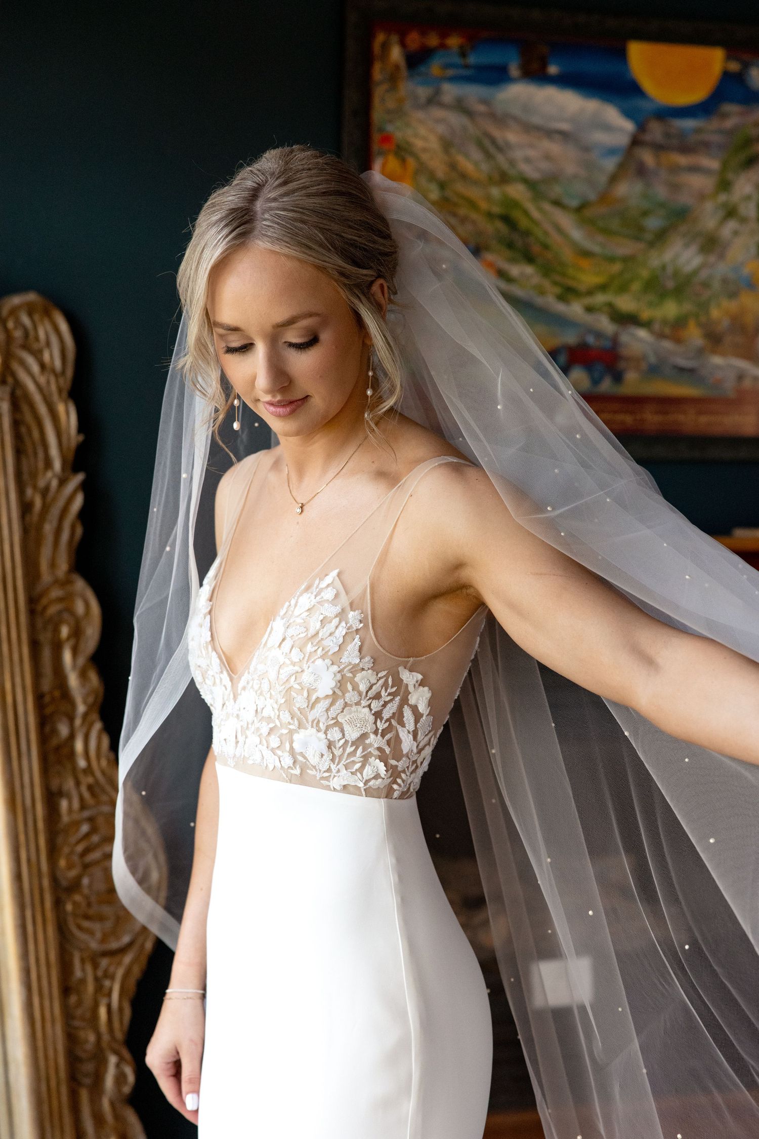 A close-up portrait of an elegant bride wearing a white lace wedding gown with delicate spaghetti straps and flowing veil.