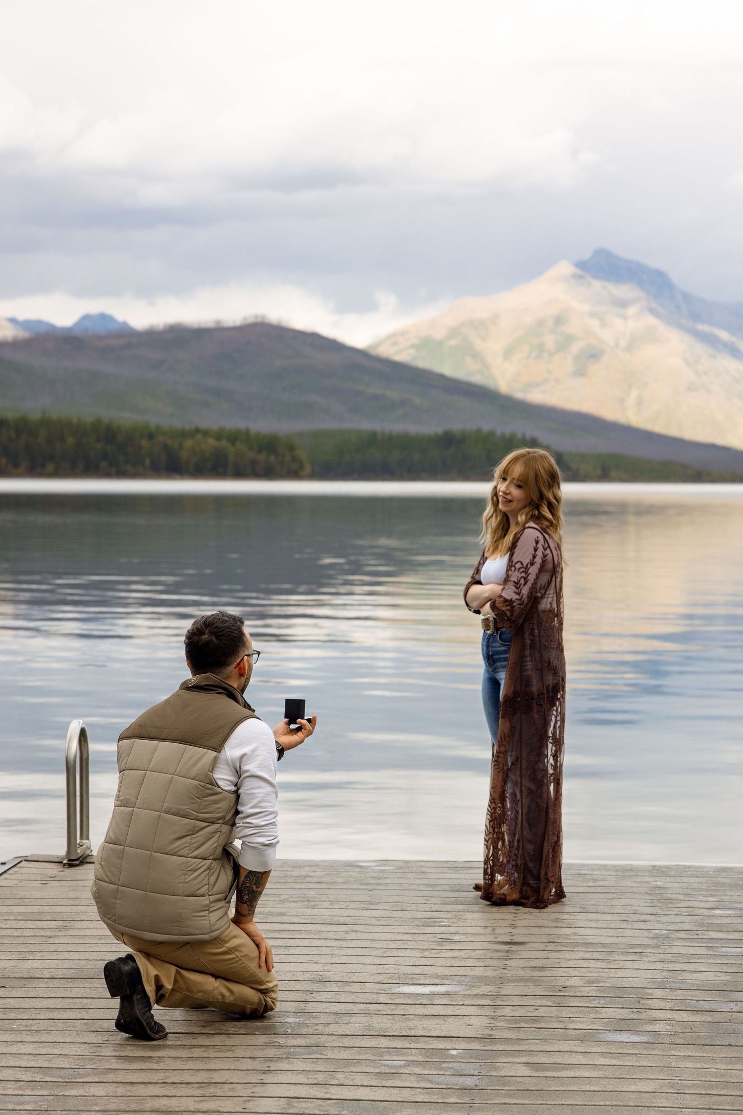 Photographer standing on wooden dock captures images of driftwood at scenic mountain lake in serene setting.
