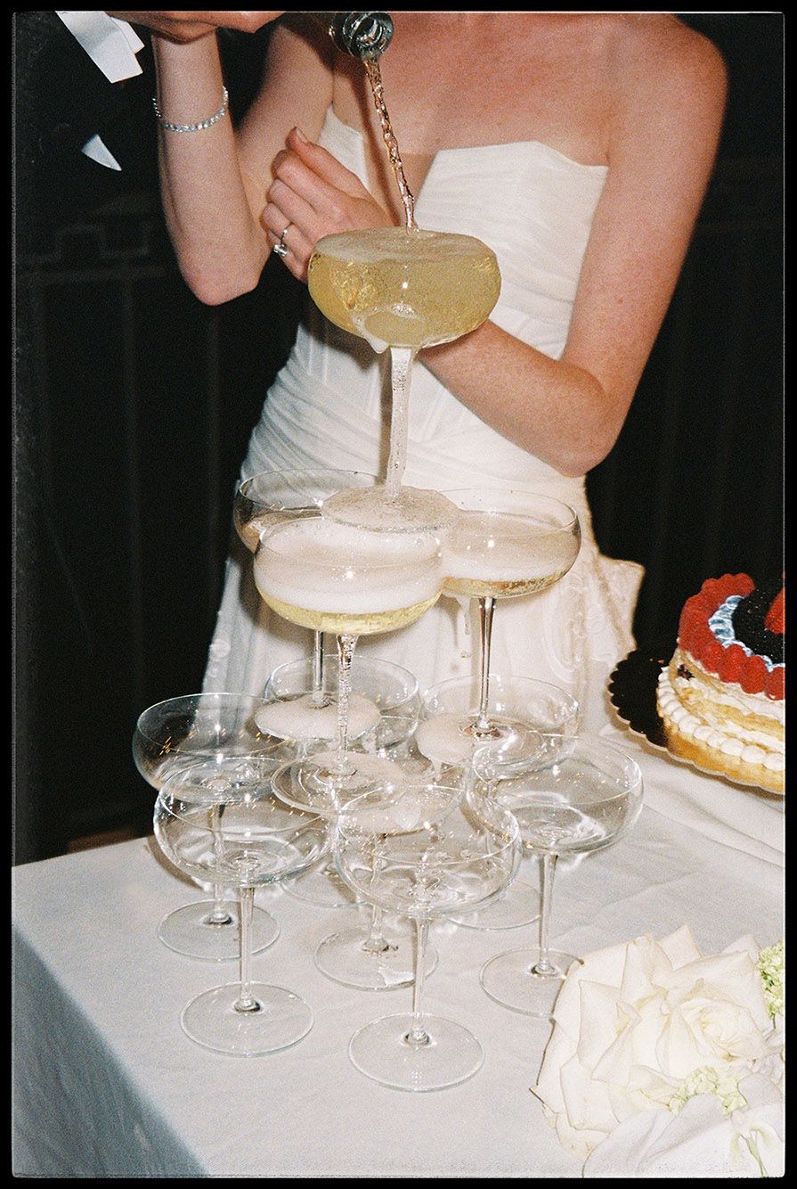 A champagne tower stack of coupe glasses set up with bubbling liquid being poured from the top at a celebration.
