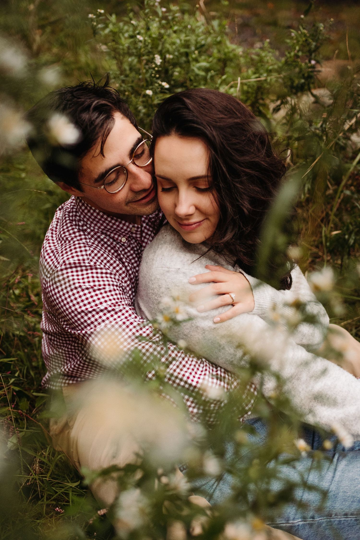 Romantic couple embracing tenderly while sitting together among wildflowers in a lush meadow.
