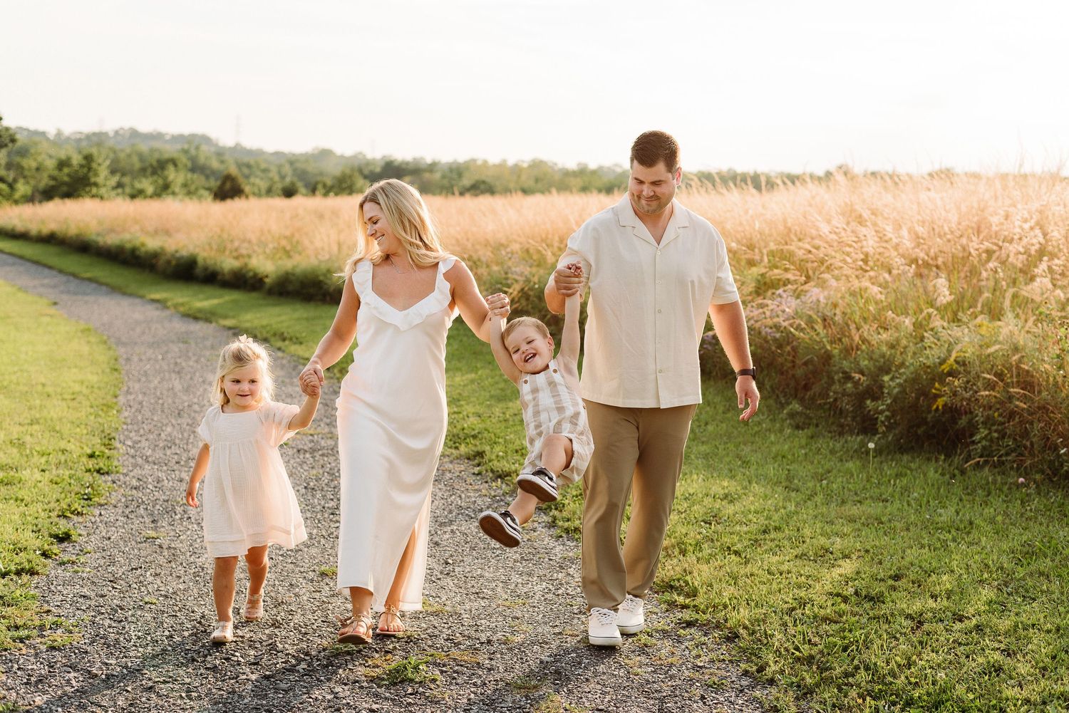Family walking together through a golden wheat field at sunset in summer while holding hands.