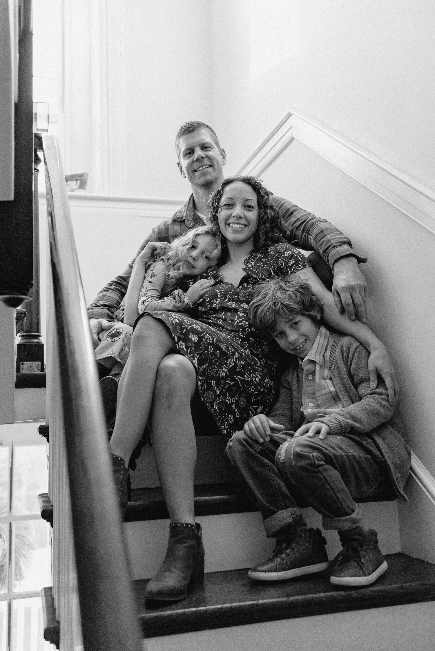 Black and white photo of family sitting together on carpeted stairs in their home in Berks County PA.