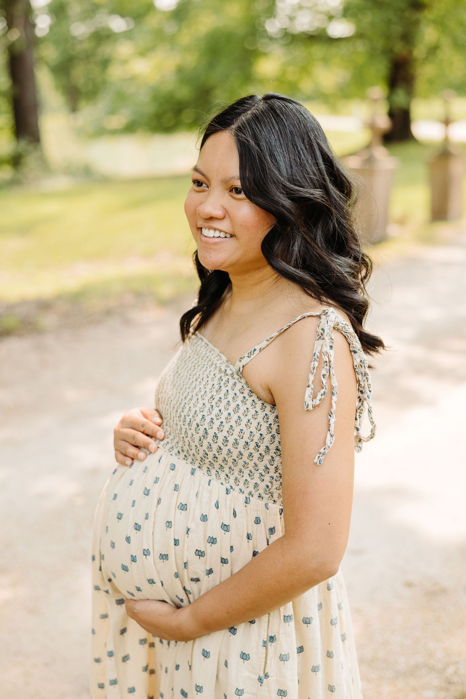 A series of maternity photos showing a pregnant person in a white floral dress smiling and posing outdoors.