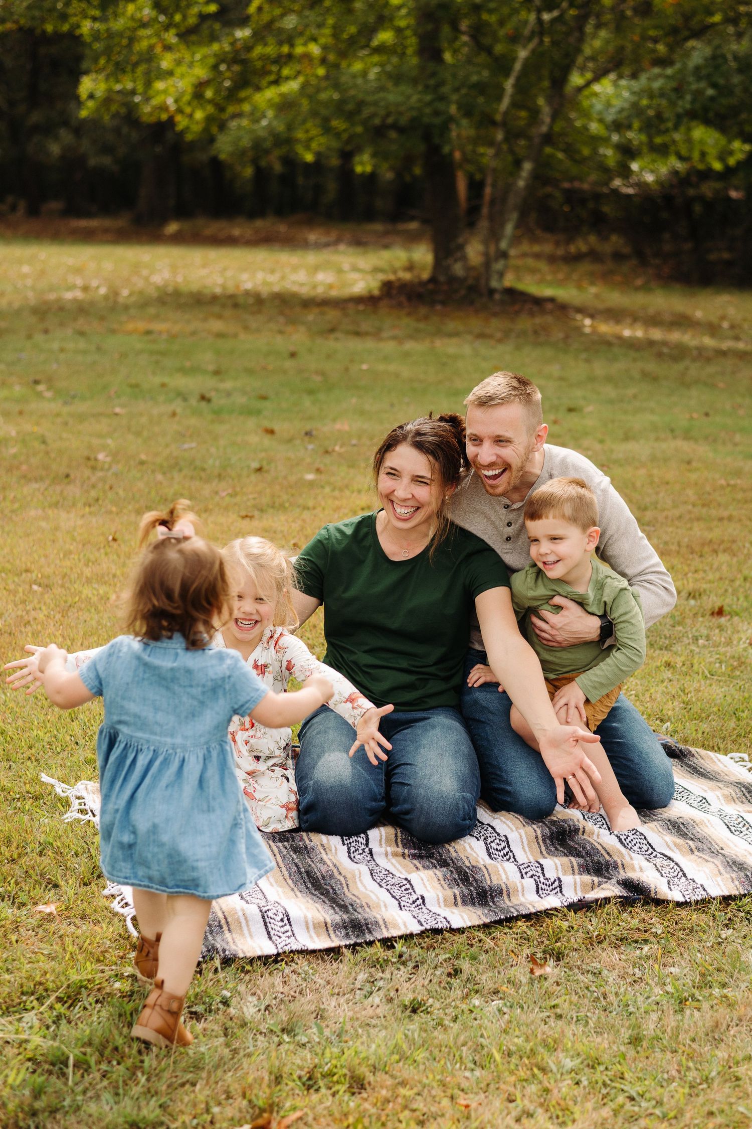Family enjoying a picnic together on a blanket in a grassy park during autumn in Pittsburgh, PA.