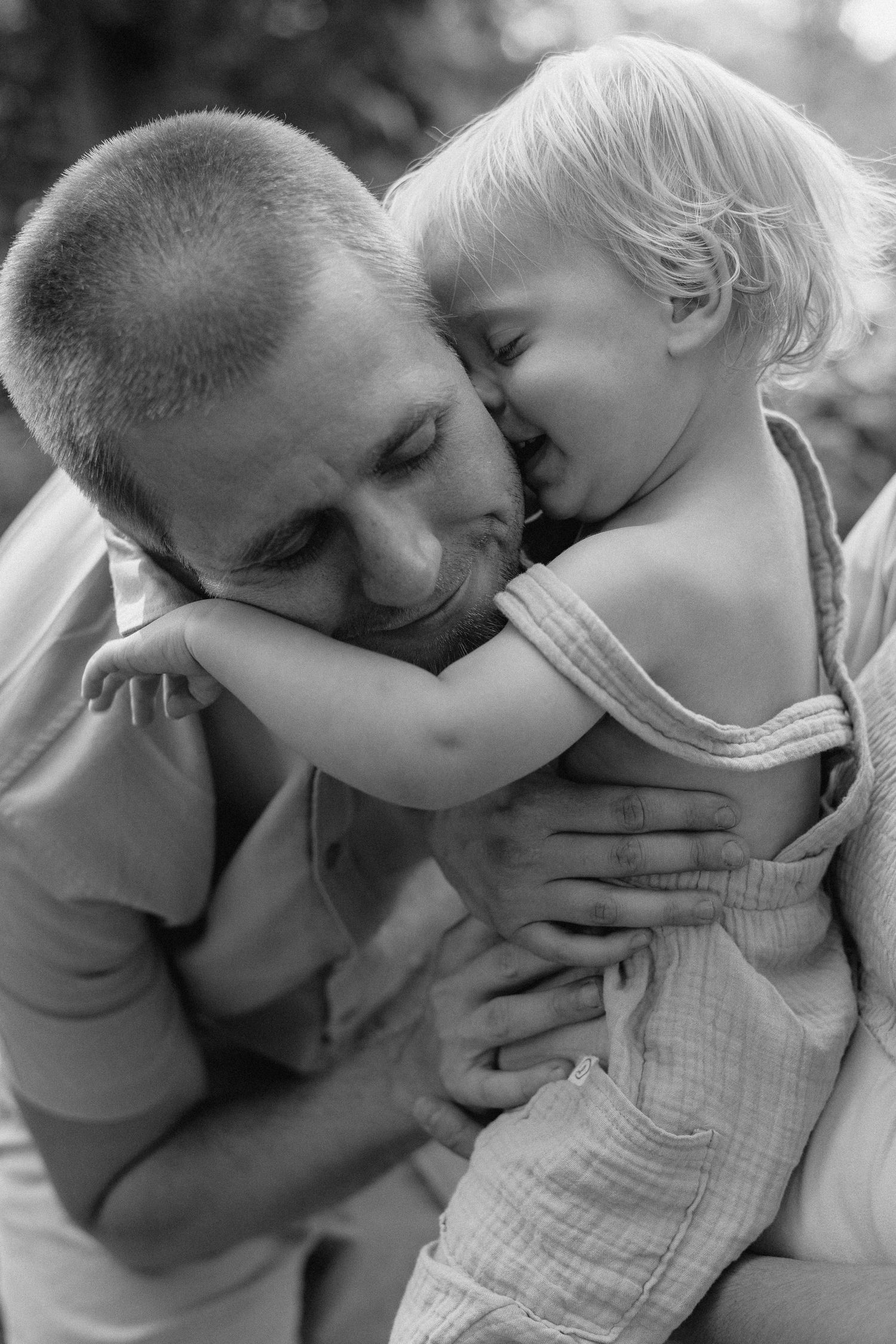A tender black and white portrait capturing an intimate moment between a parent and young child in an outdoor setting.