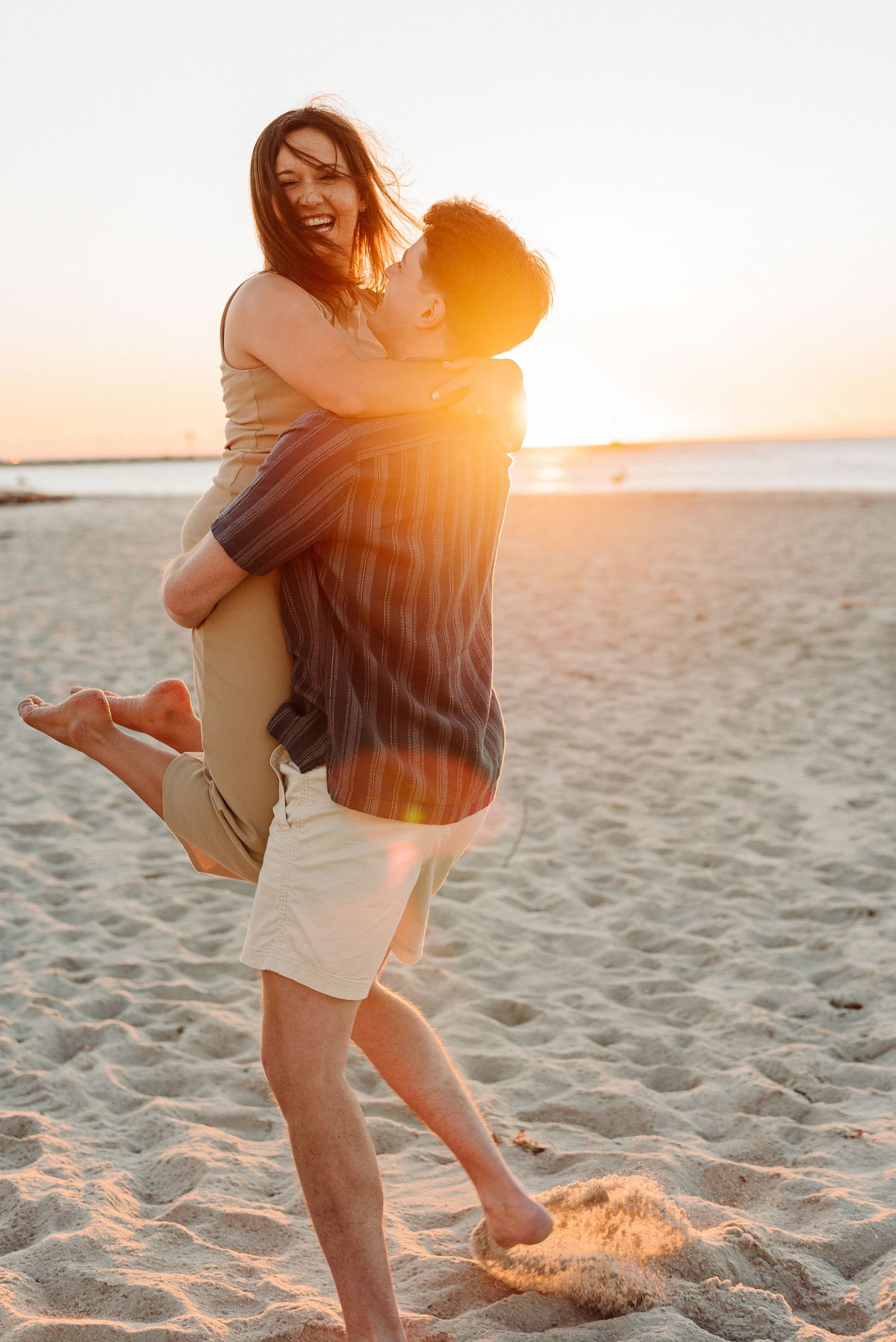 Romantic couple embracing on sandy beach at sunset with golden sunlight streaming through their silhouettes.