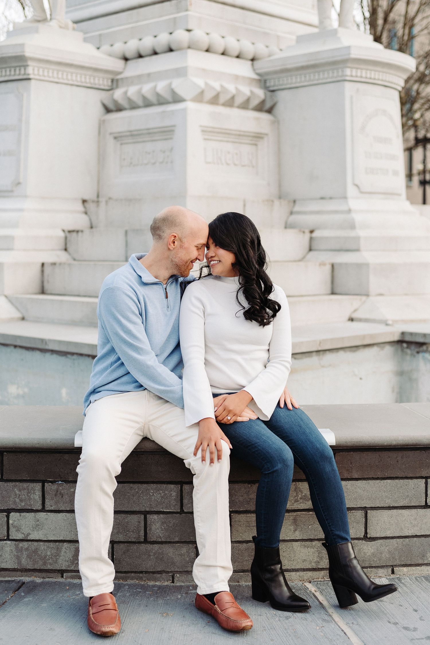 A couple shares a tender moment while sitting on stone steps against white architectural columns in Easton, PA.