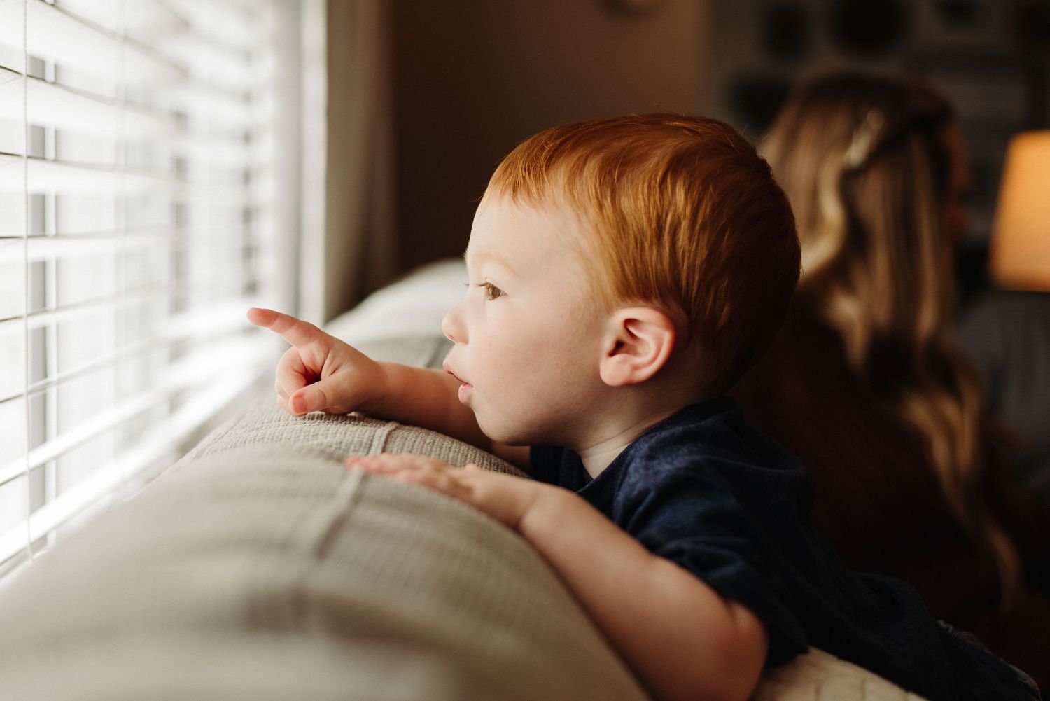 A child sits by a window with sunlight streaming in, creating a warm and contemplative atmosphere.