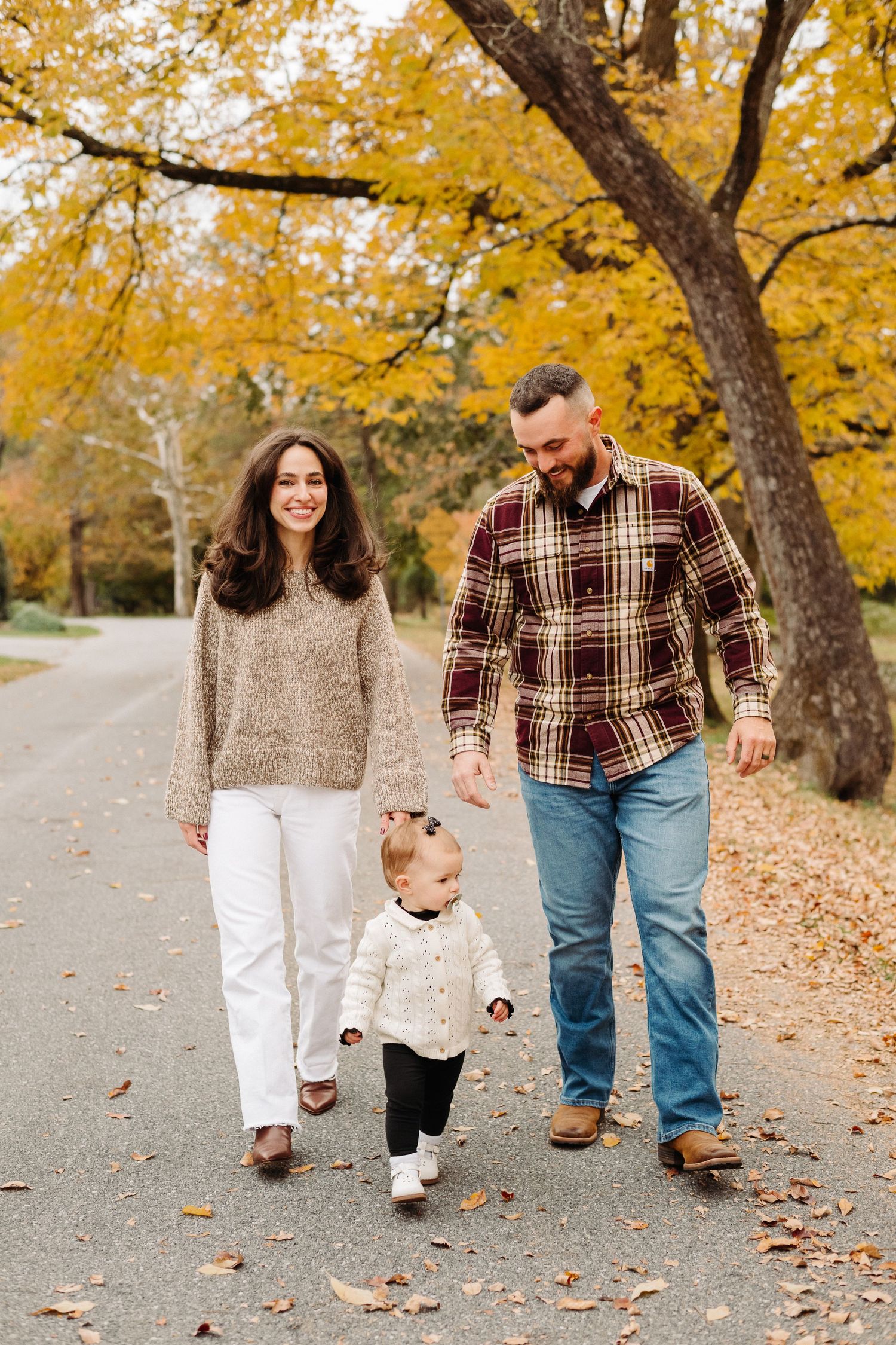 A family walks together on a path covered in fallen autumn leaves while holding hands during a fall photoshoot in Wyomissing PA.