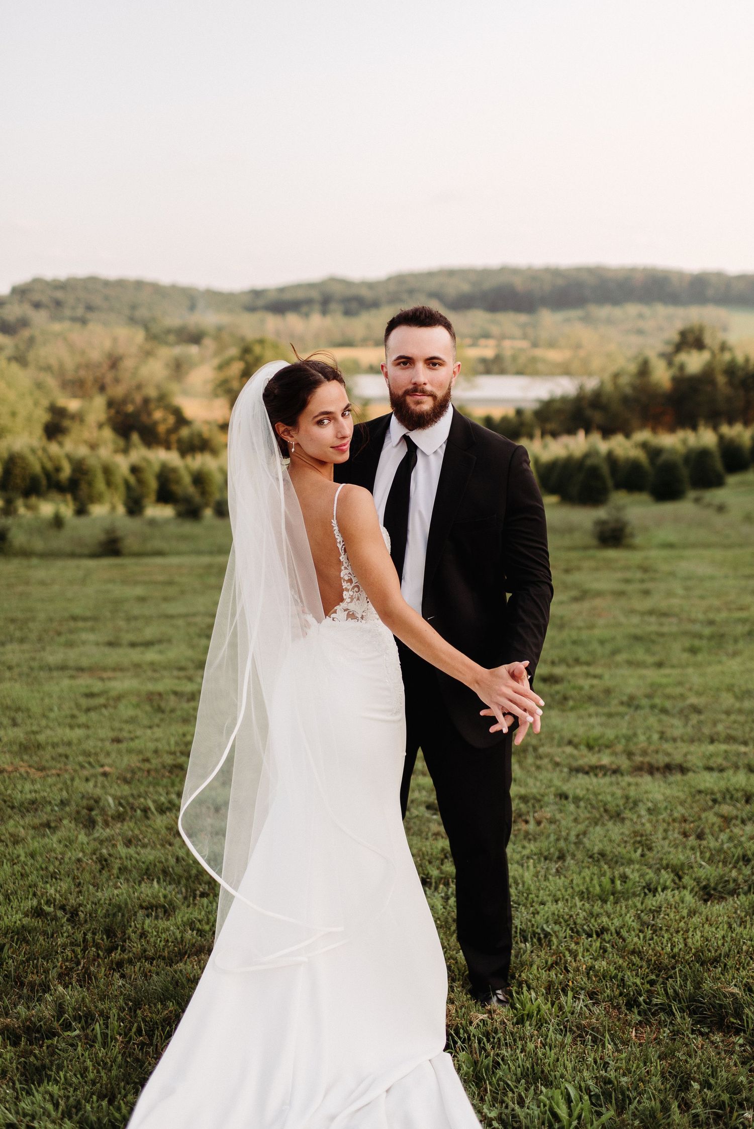 A couple in wedding attire poses together in a scenic green meadow during golden hour in Berks County PA.