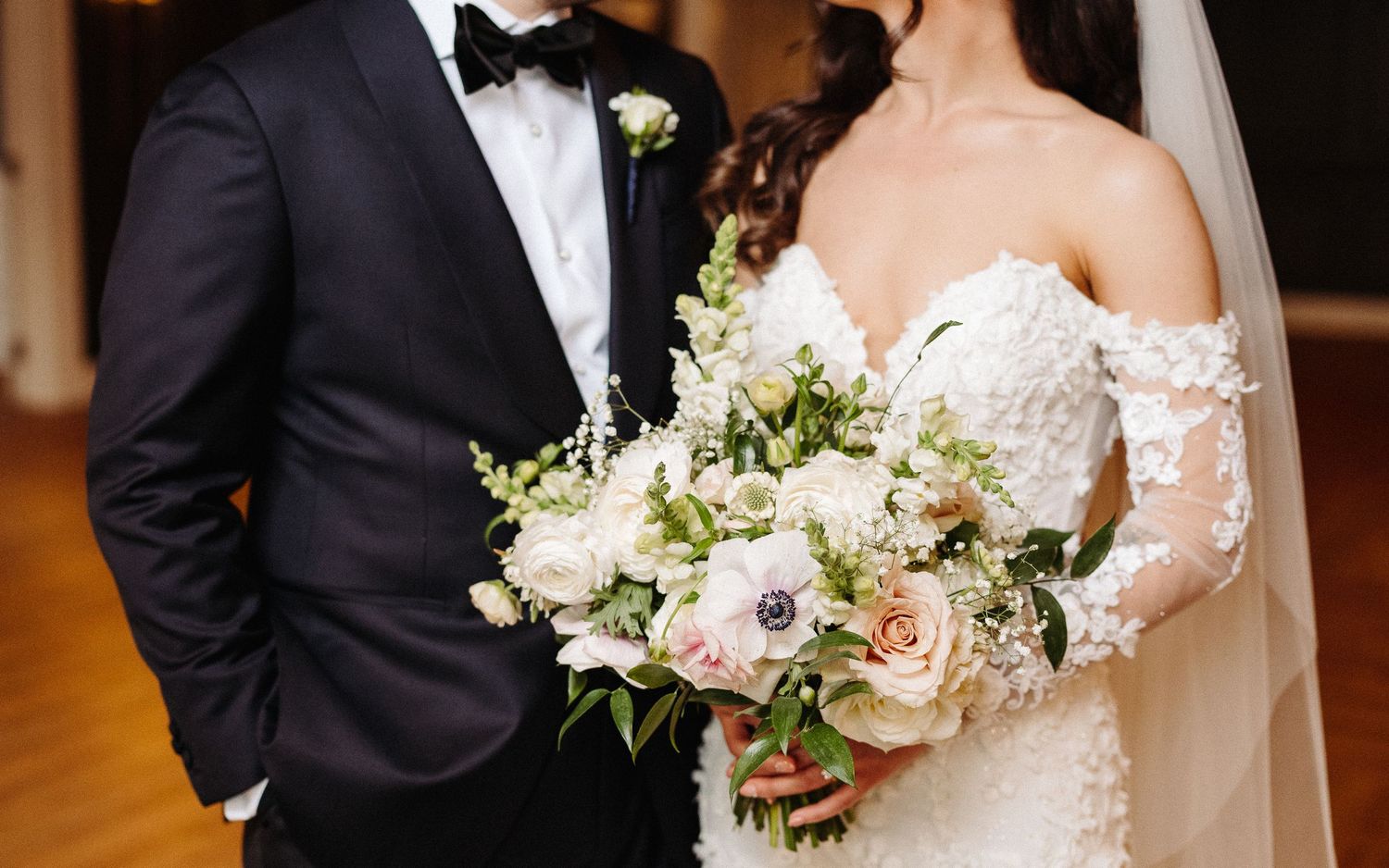 A couple in formal wedding attire holds hands and embraces during their elegant indoor ceremony.