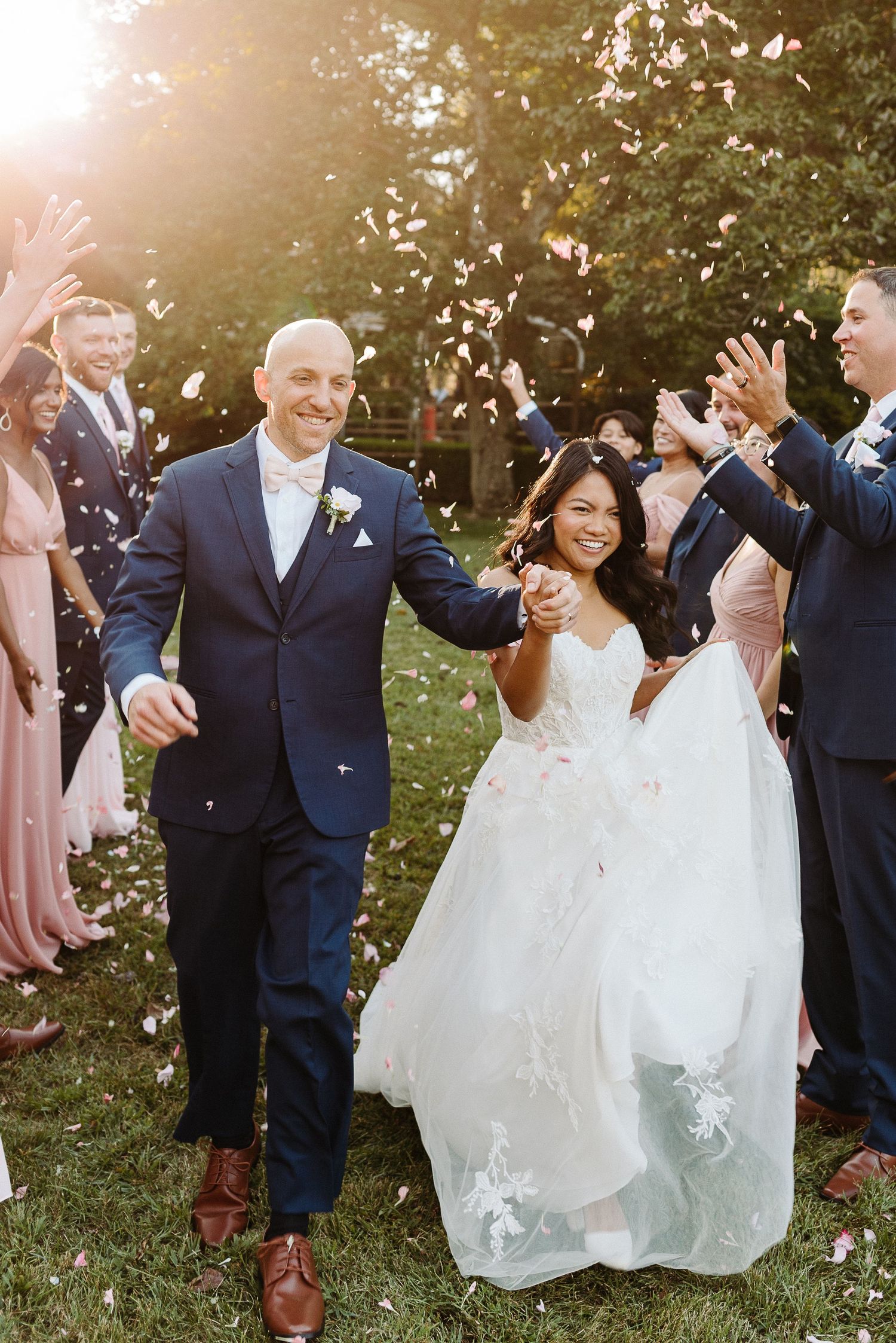 Wedding guests toss white flower petals at a joyful couple celebrating their marriage in an outdoor garden setting.