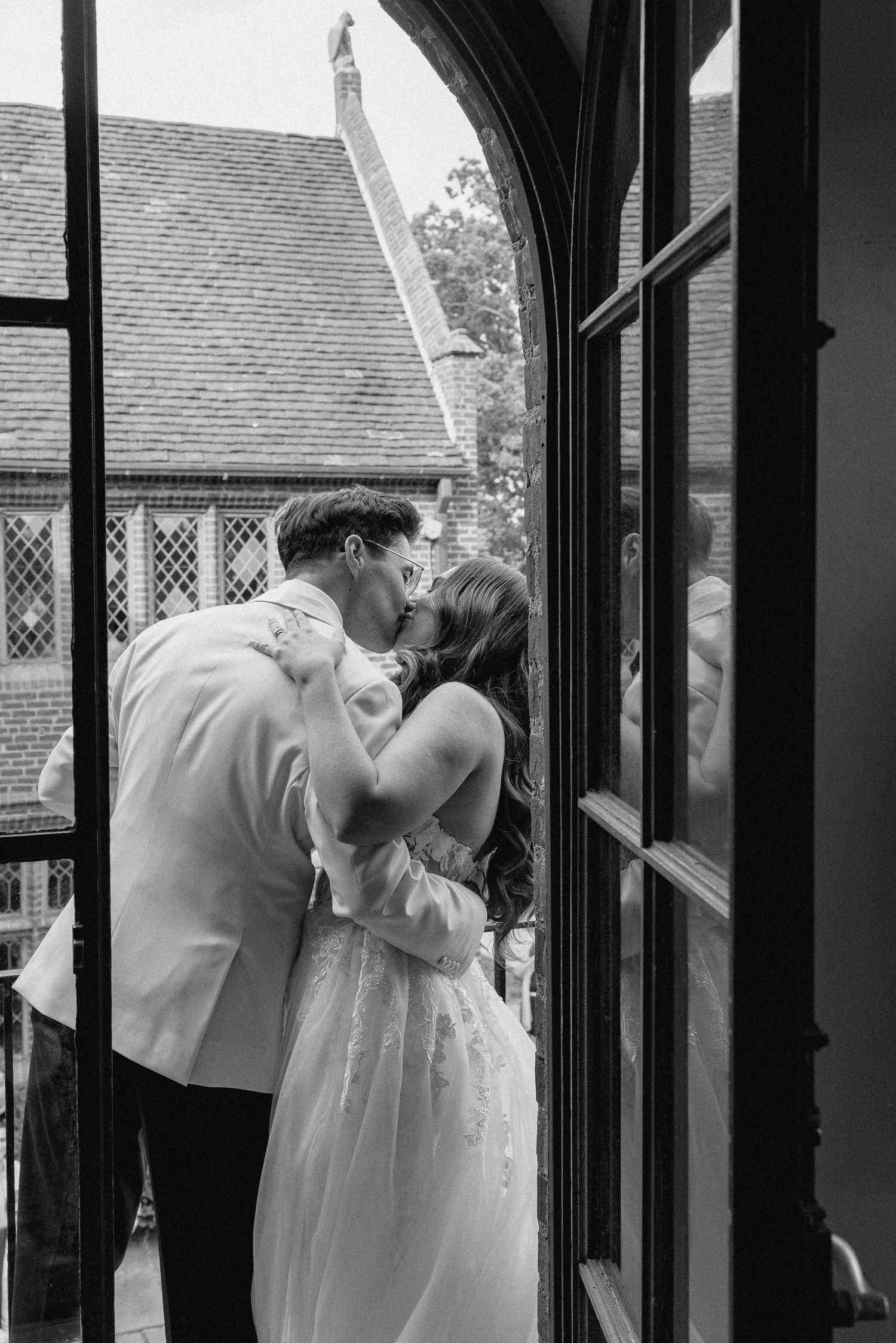 A couple shares a romantic kiss in a black and white photo framed by architectural columns and windows in Lehigh County, PA.
