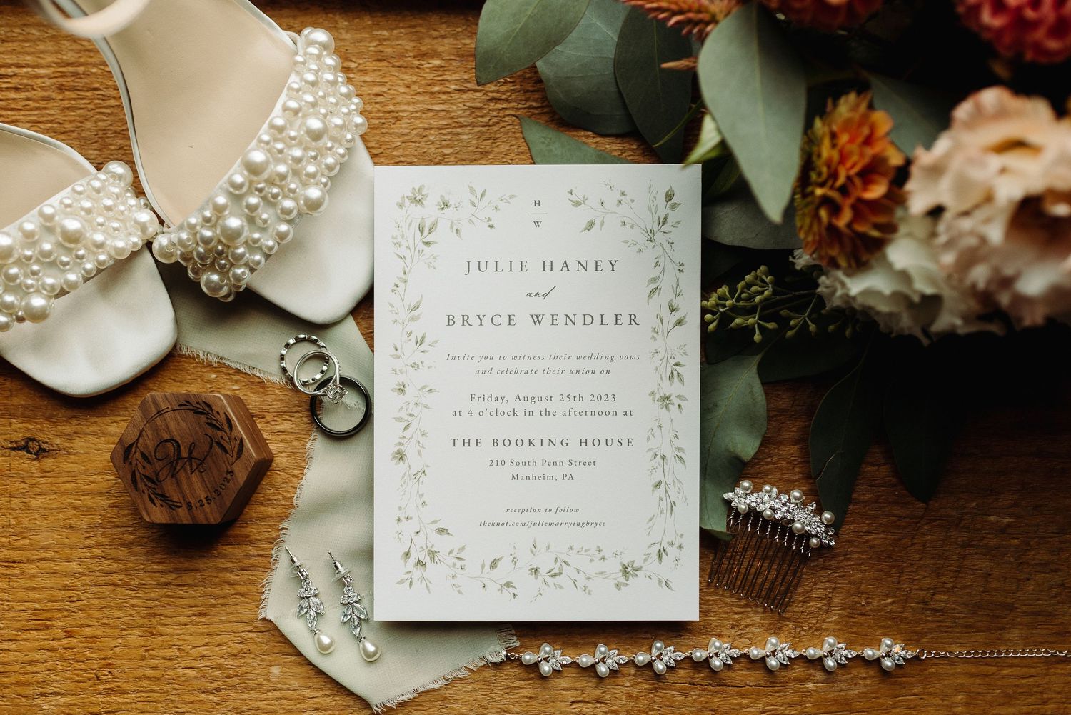 Elegant wedding invitations and jewelry laid out on rustic wooden surface with delicate floral decorations. Manheim, PA