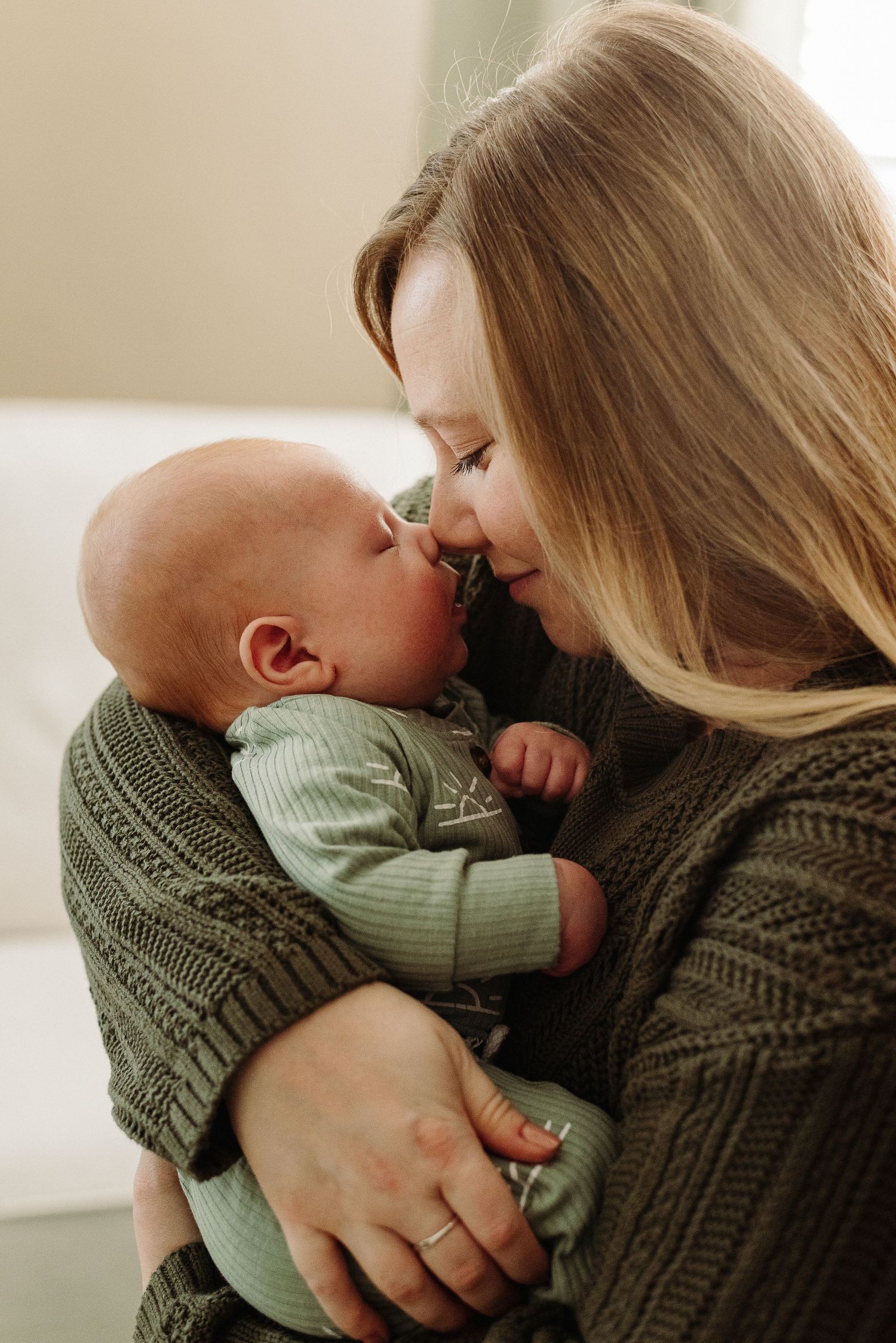 A tender moment between parent and baby wearing olive green and brown knit sweaters.
