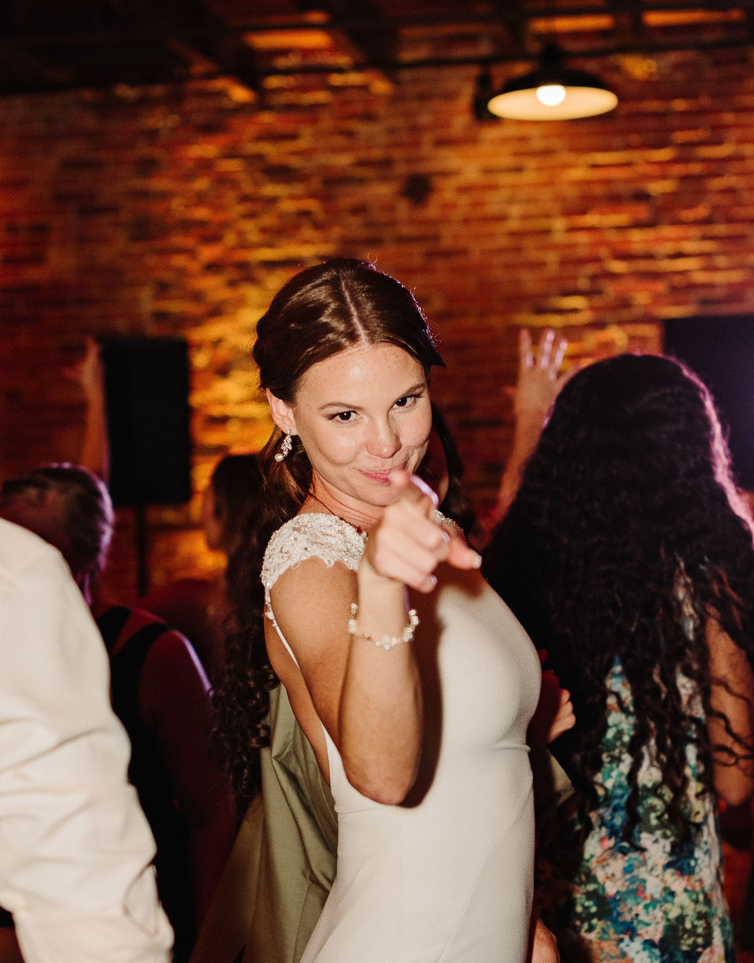 A sequence of dance floor moments showing guests celebrating at an indoor reception venue with exposed brick walls and warm lighting.