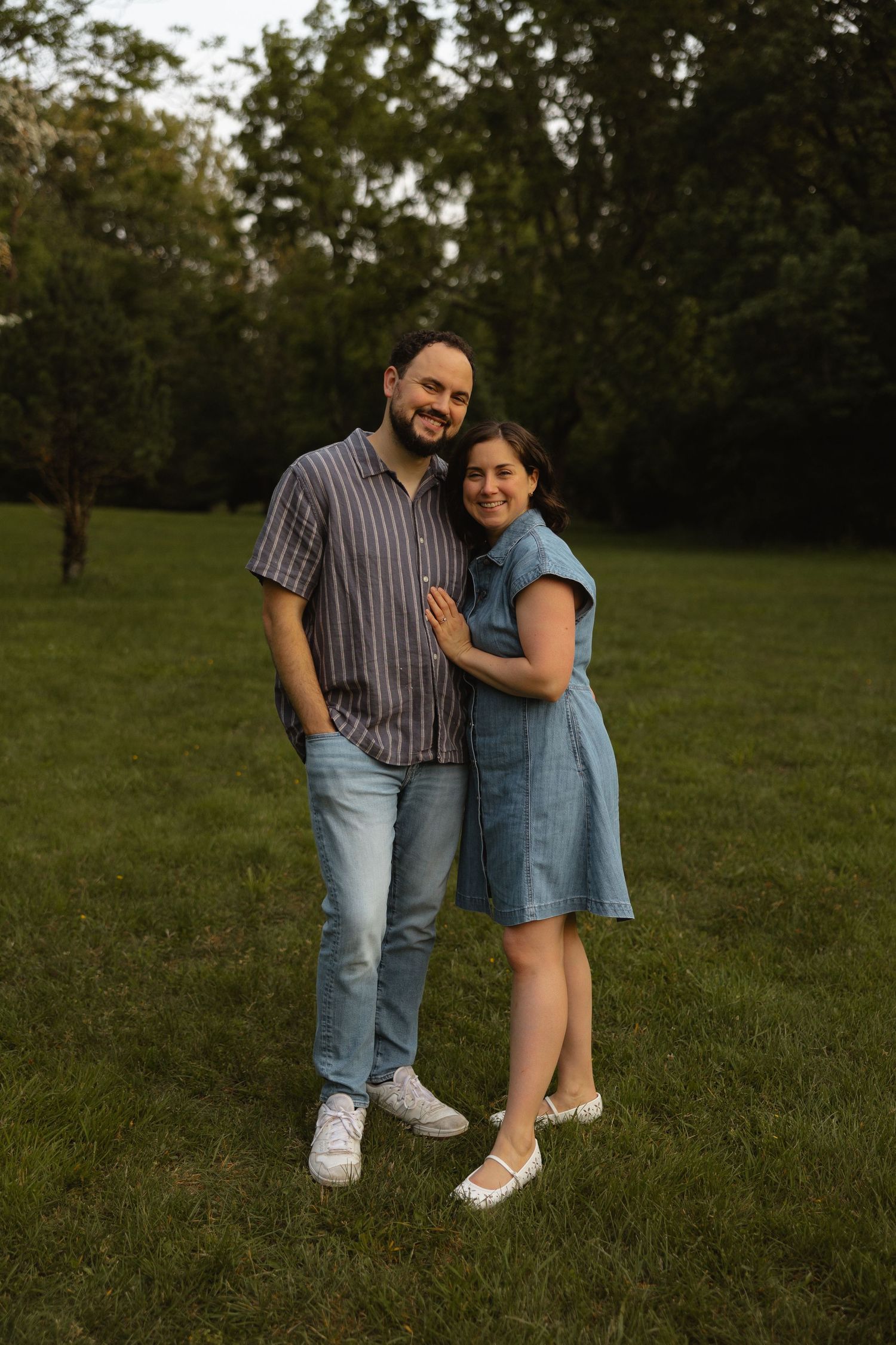 A couple embraces while standing in a grassy field during golden hour.