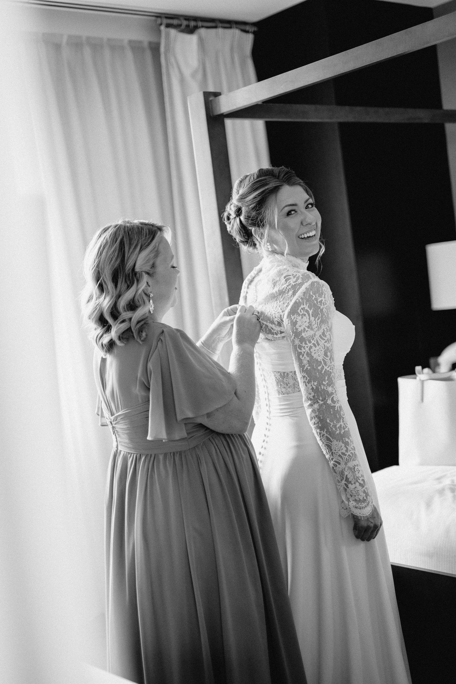 A row of bridesmaid dresses in soft gray tones hang beside a white wedding gown in a bridal suite.