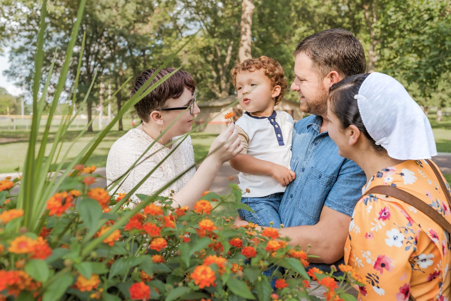 Happy family with young child admiring orange flowers together in a lush green park on a sunny day.
