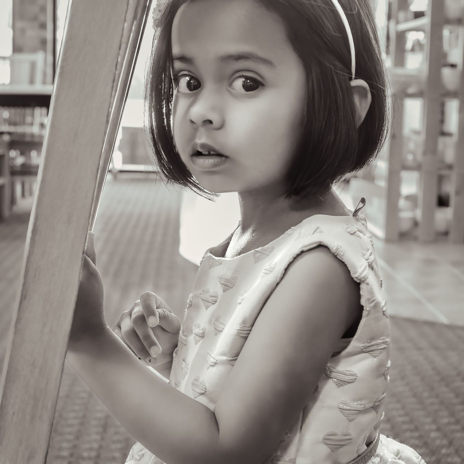Black and white portrait of a young girl with a bob haircut in a white dress at a playground.