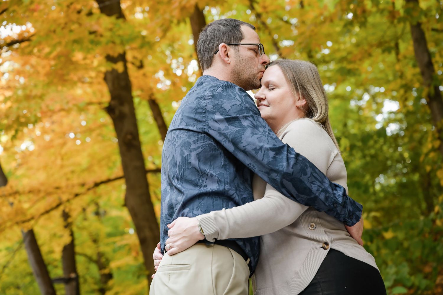Couple embracing romantically among colorful autumn foliage in a forest setting.