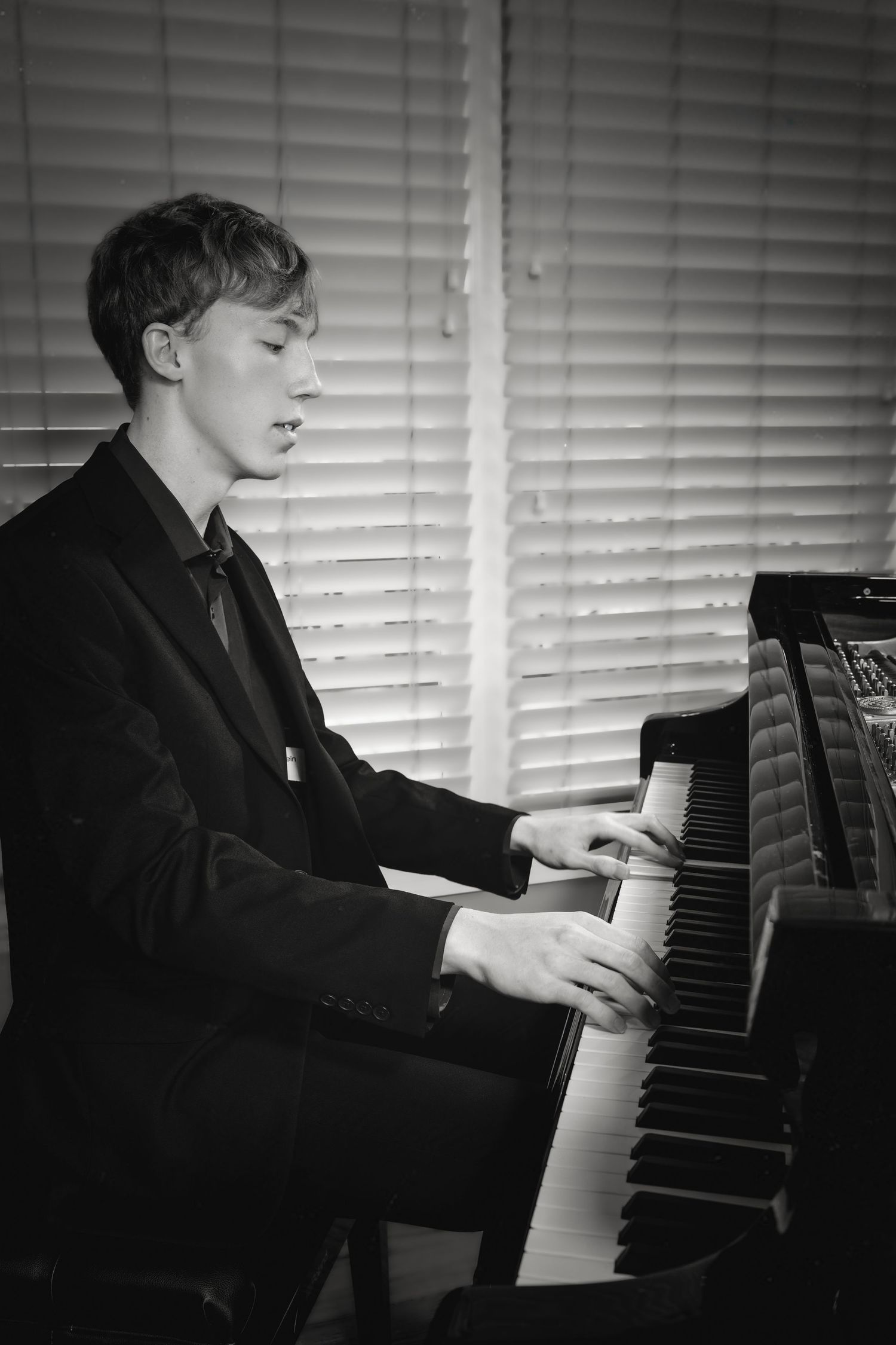 Black and white photo of a teenage boy playing piano in formal attire.