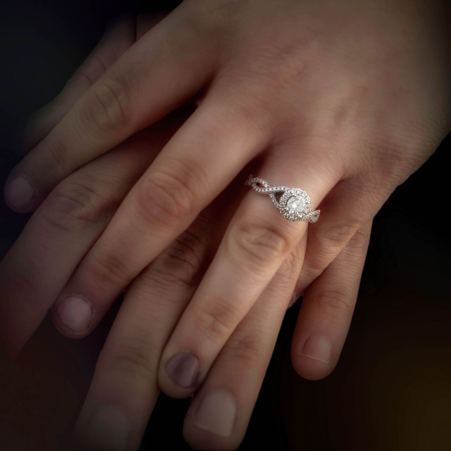 Close-up of diamond halo engagement ring on woman's finger held by partner.