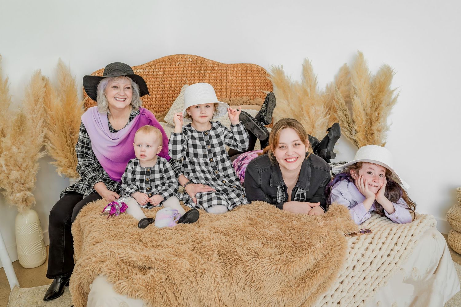 Group of five girls posing together on cozy bed with boho pampas grass decor backdrop.