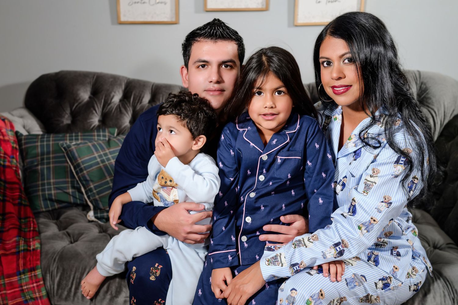 Family of four in matching navy blue pajamas posing together on a gray tufted sofa.
