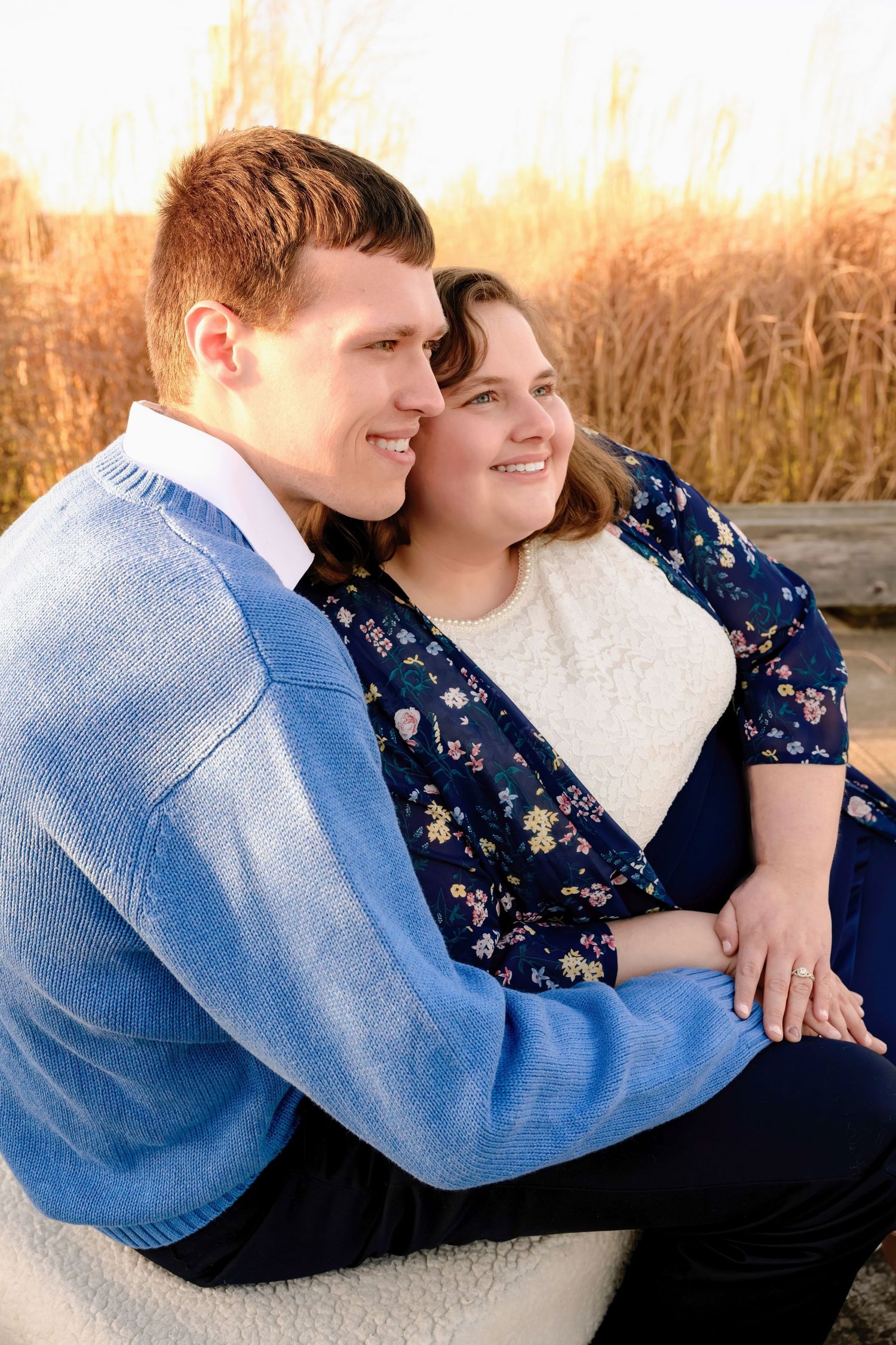 Young couple sitting closely together smiling at sunset near tall golden grasses.