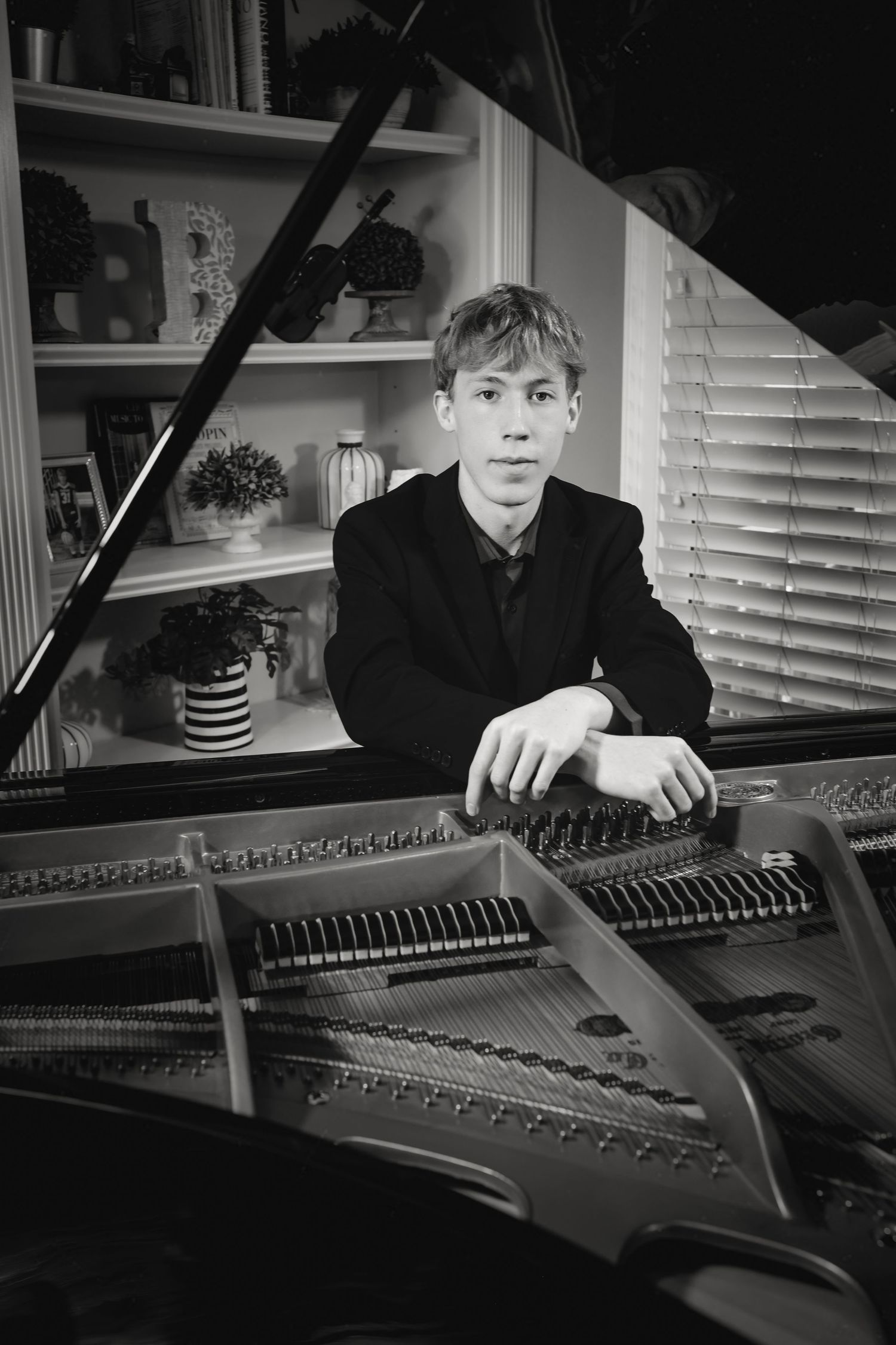 Young male pianist in black suit posing with open grand piano in elegant home setting.