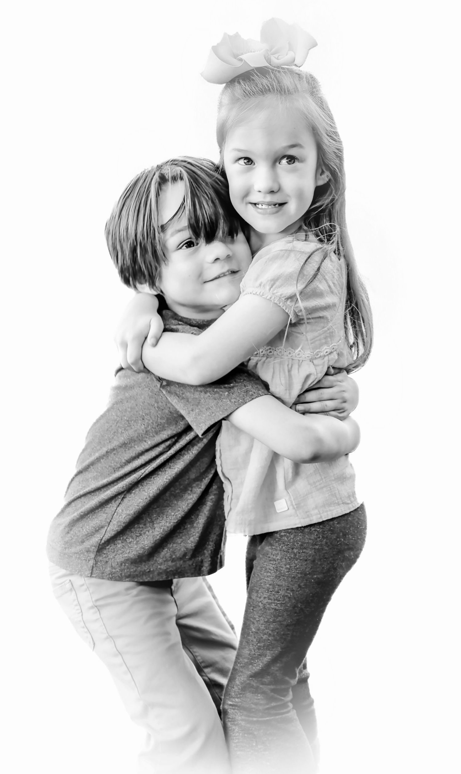 Black and white portrait of two young siblings hugging and smiling in a studio setting.