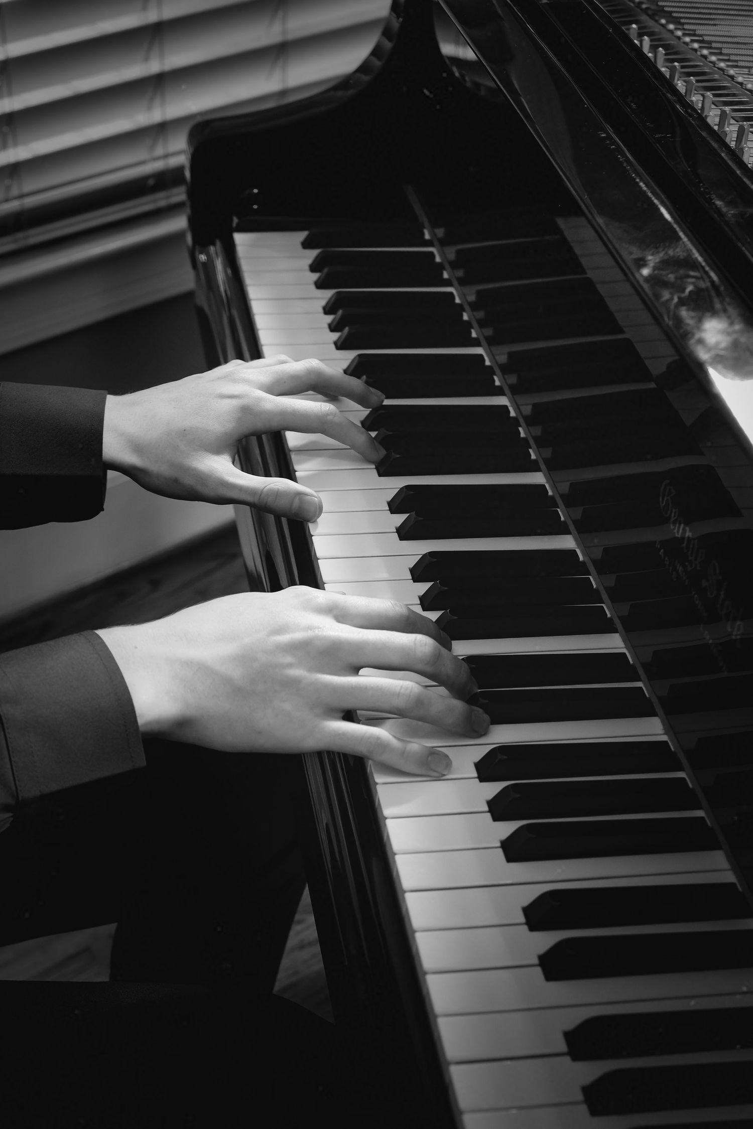 Black and white close-up of pianist hands playing grand piano keys in formal attire.
