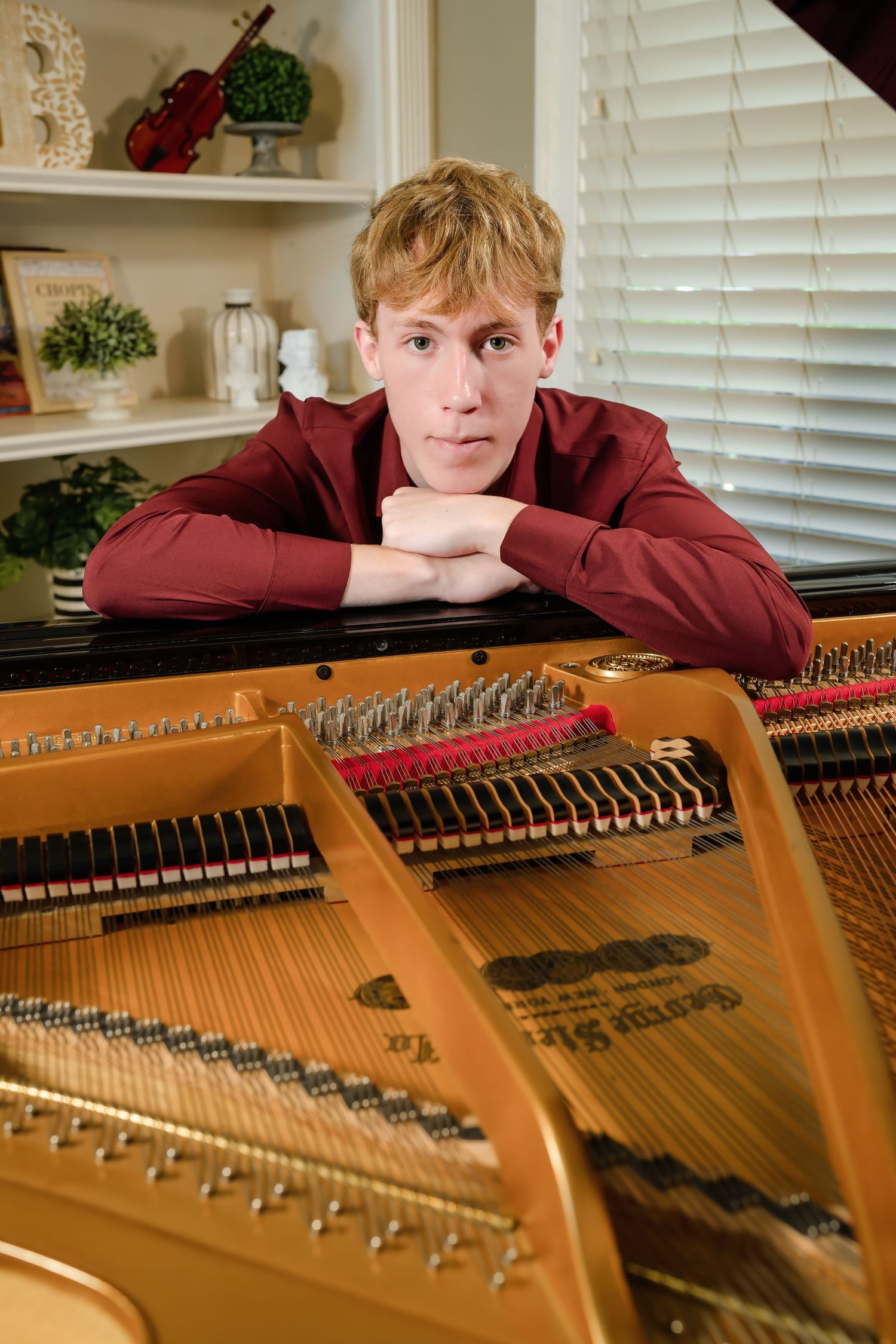 Young male pianist in red shirt resting chin on arms over open grand piano.