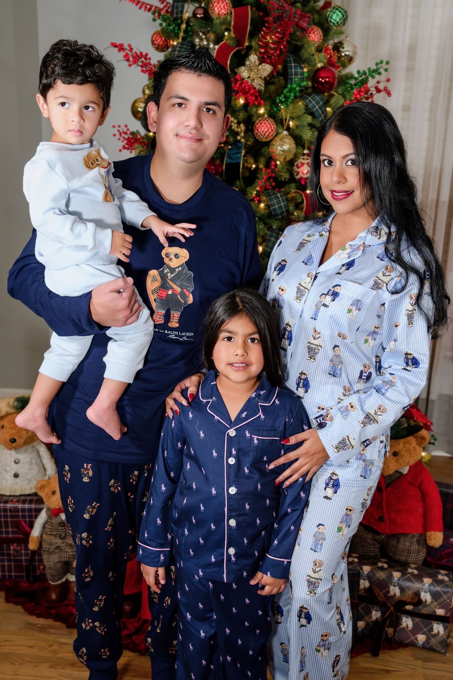 Family of four in matching Polo pajamas posing by decorated Christmas tree.