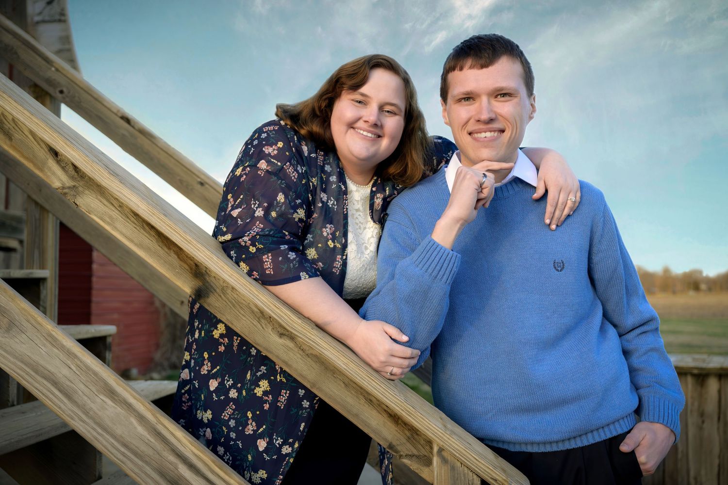 Smiling couple posing together on wooden staircase outdoors at sunset.