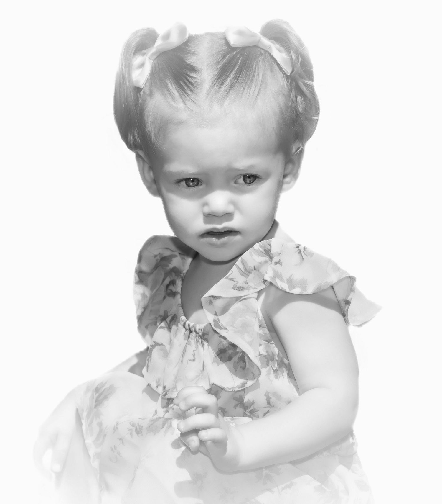 Black and white portrait of a toddler girl with pigtails wearing a ruffled floral dress.