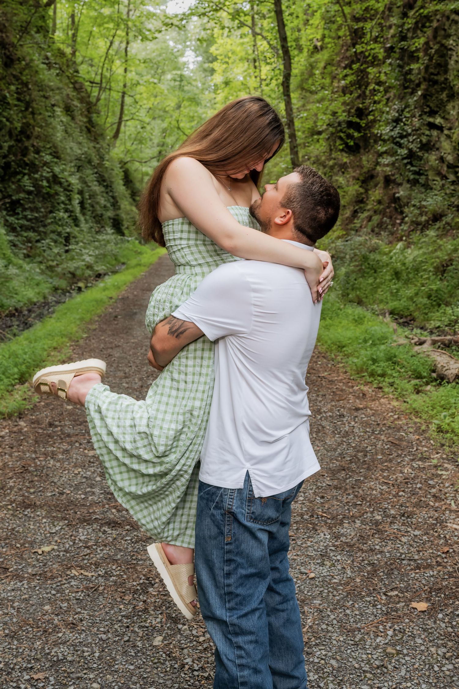 A couple sharing a romantic kiss on a forest path, man lifting woman in green dress.